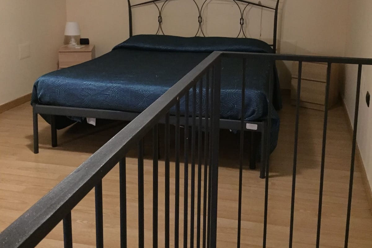 Un dormitorio con cama, mesita de noche, lámpara y equipo de aire acondicionado en la pared.