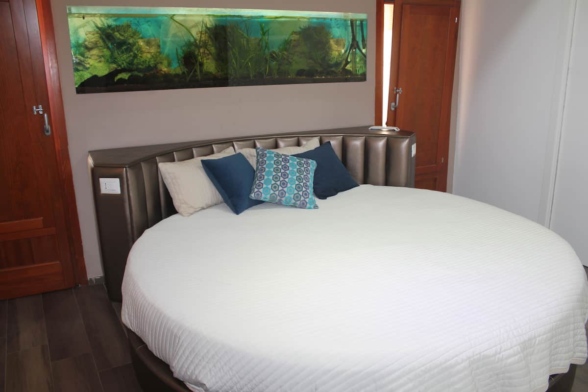 Un dormitorio con una cama grande, cabecera y un acuario fijado a la pared.