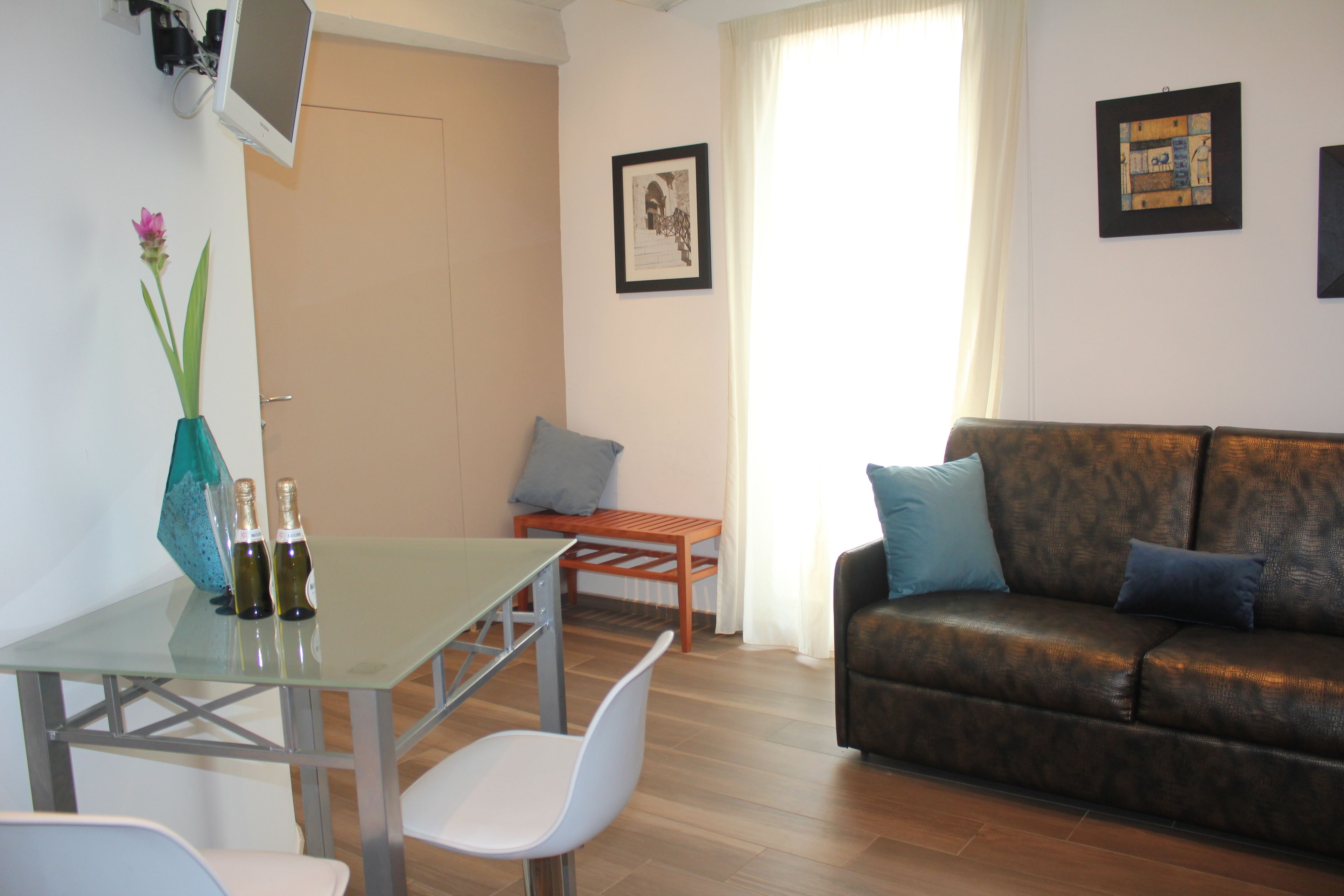 A modern living room with a glass table, white chairs, a brown leather sofa, and a wooden bench.