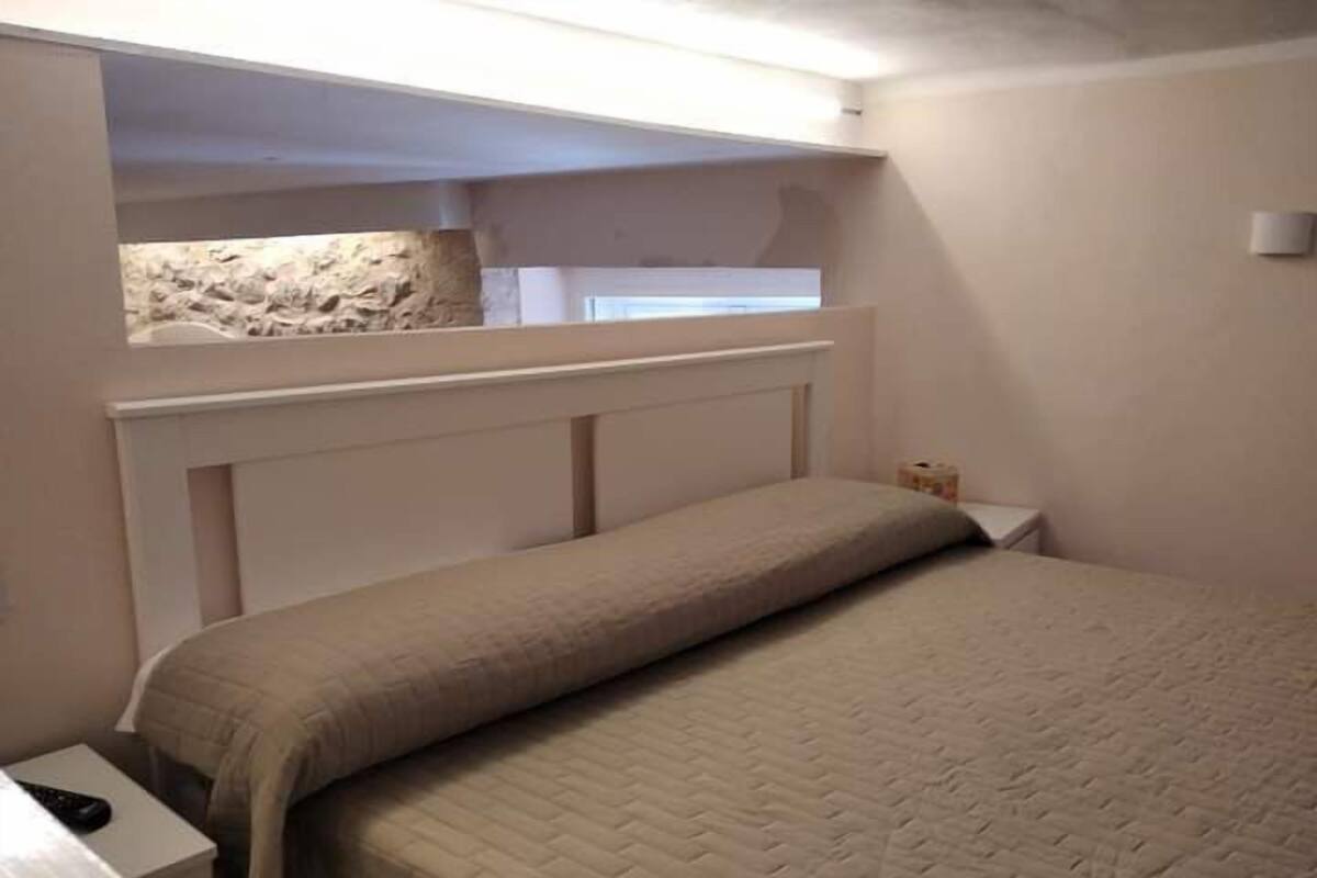 Un dormitorio con cama, mesita de noche, una pequeña mesa y un revestimiento de pared de piedra.