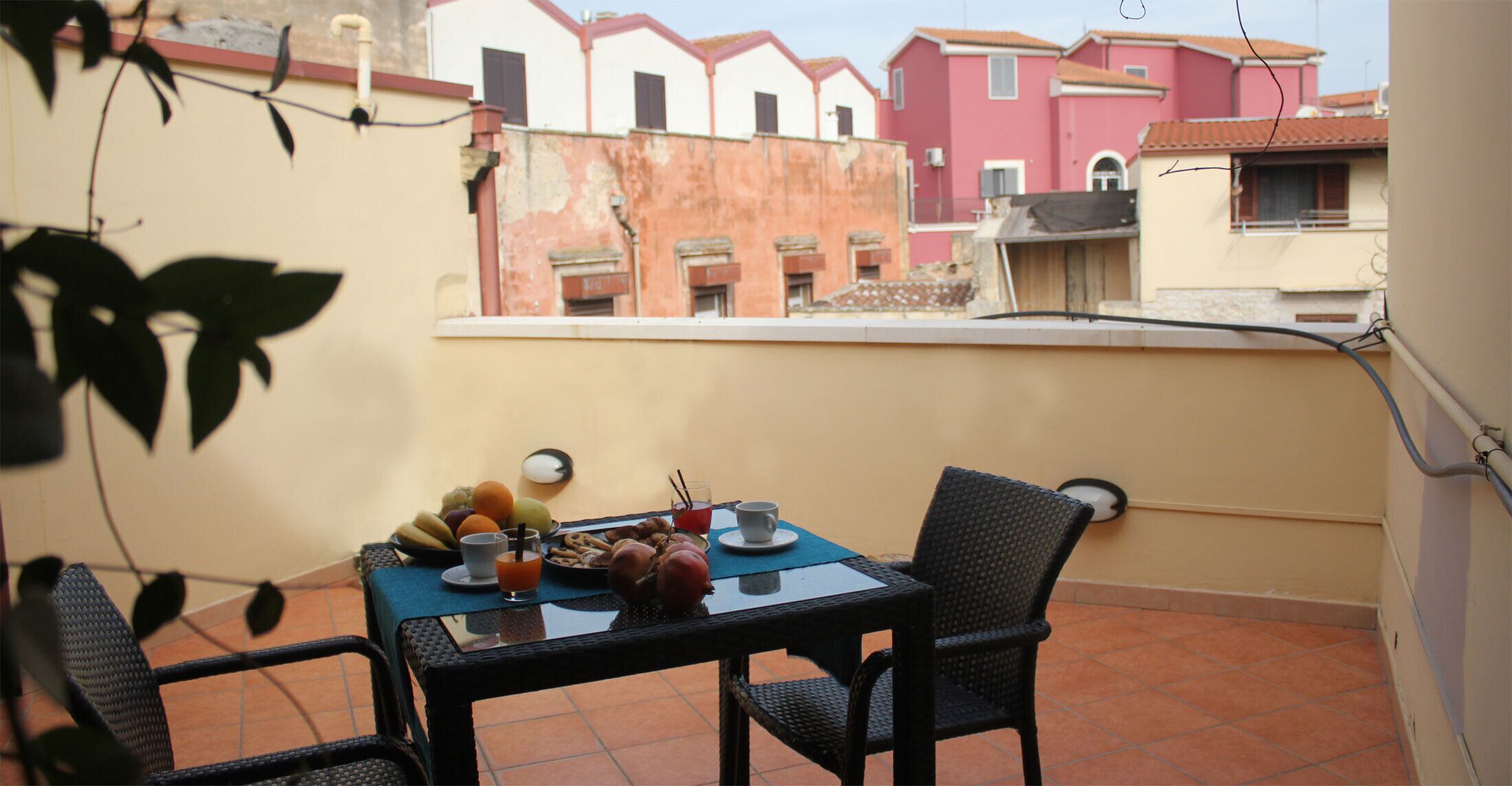 Un balcón con una mesa dispuesta para el desayuno, que incluye frutas, pan y bebidas.