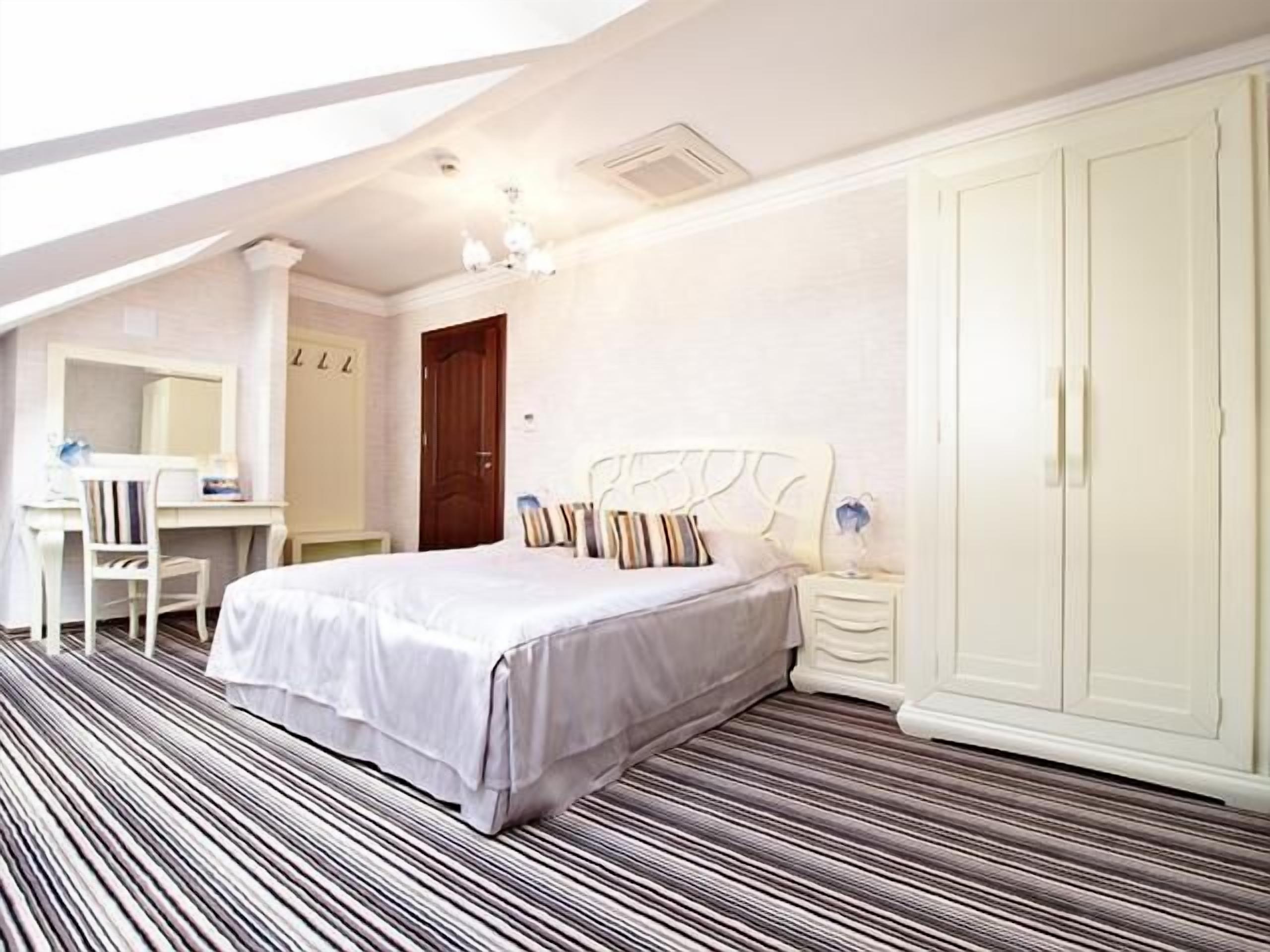 A bedroom with a bed, a desk, a chair, a wardrobe, and a striped floor.