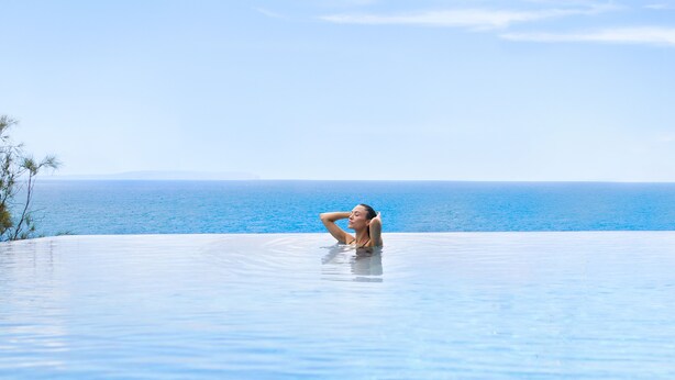 A person relaxing in a clear blue infinity pool with a view of the ocean.