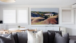 A living room with a gray sofa, a dining table with chairs, and a painting of a landscape on the wall.