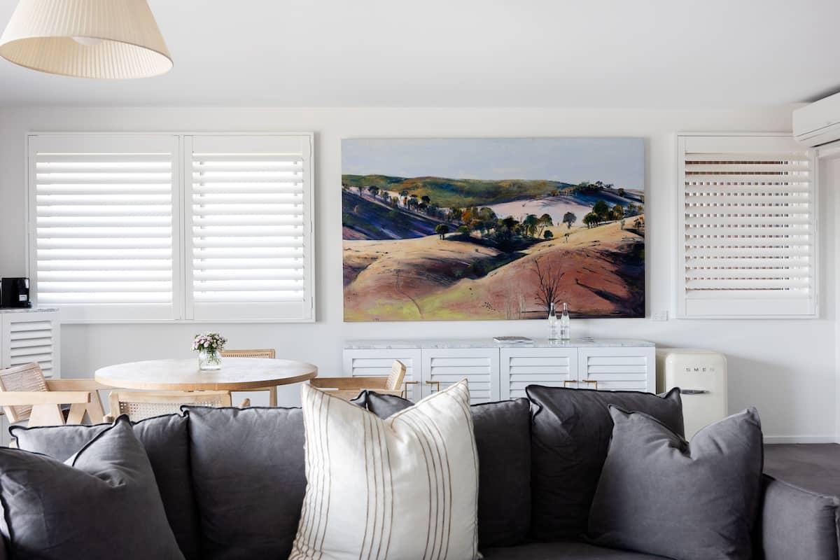 Ein Wohnzimmer mit grauem Sofa, einem Esstisch mit Stühlen und einem Landschaftsbild an der Wand.