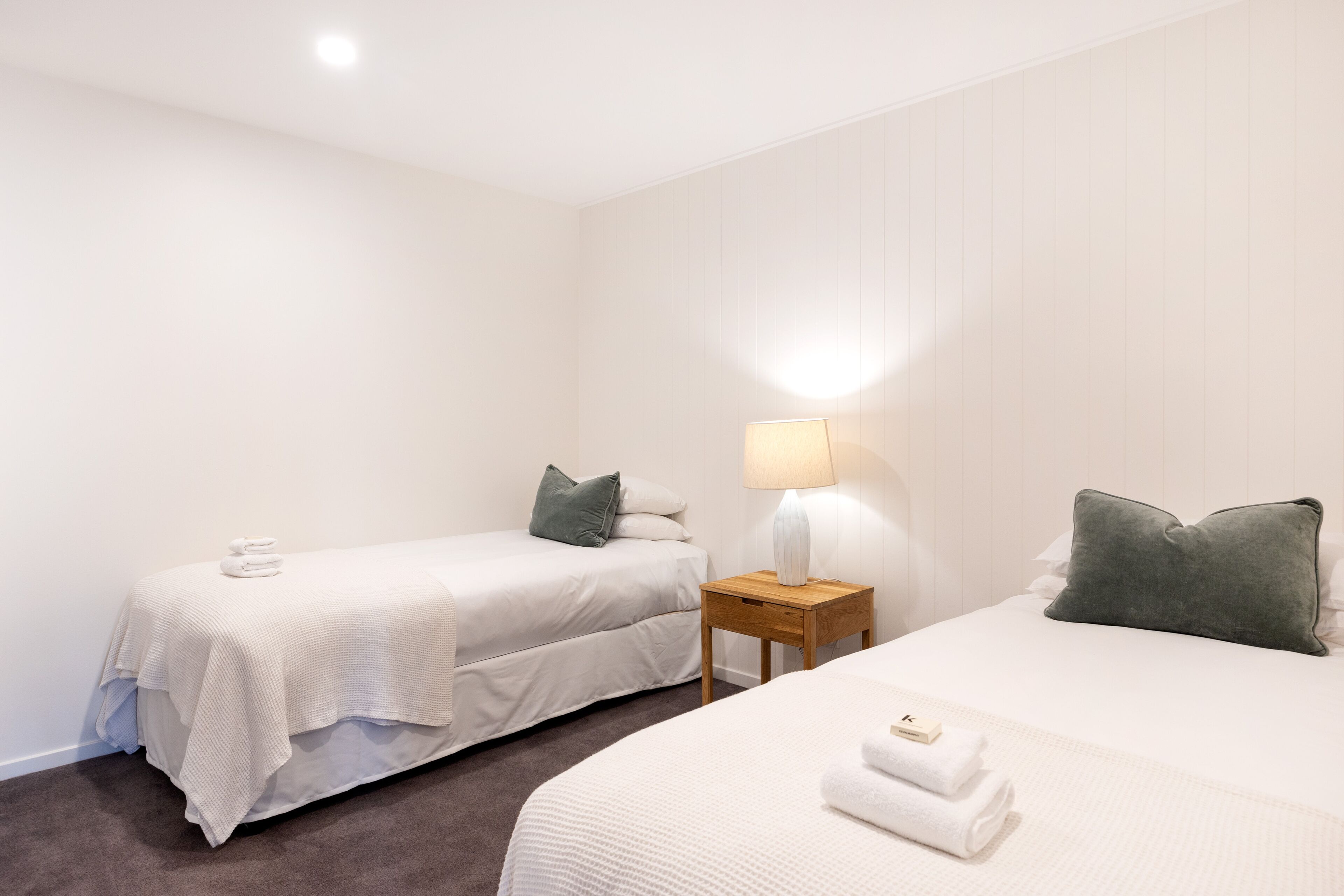 A hotel room with two beds, a nightstand with a lamp, and towels on the beds.