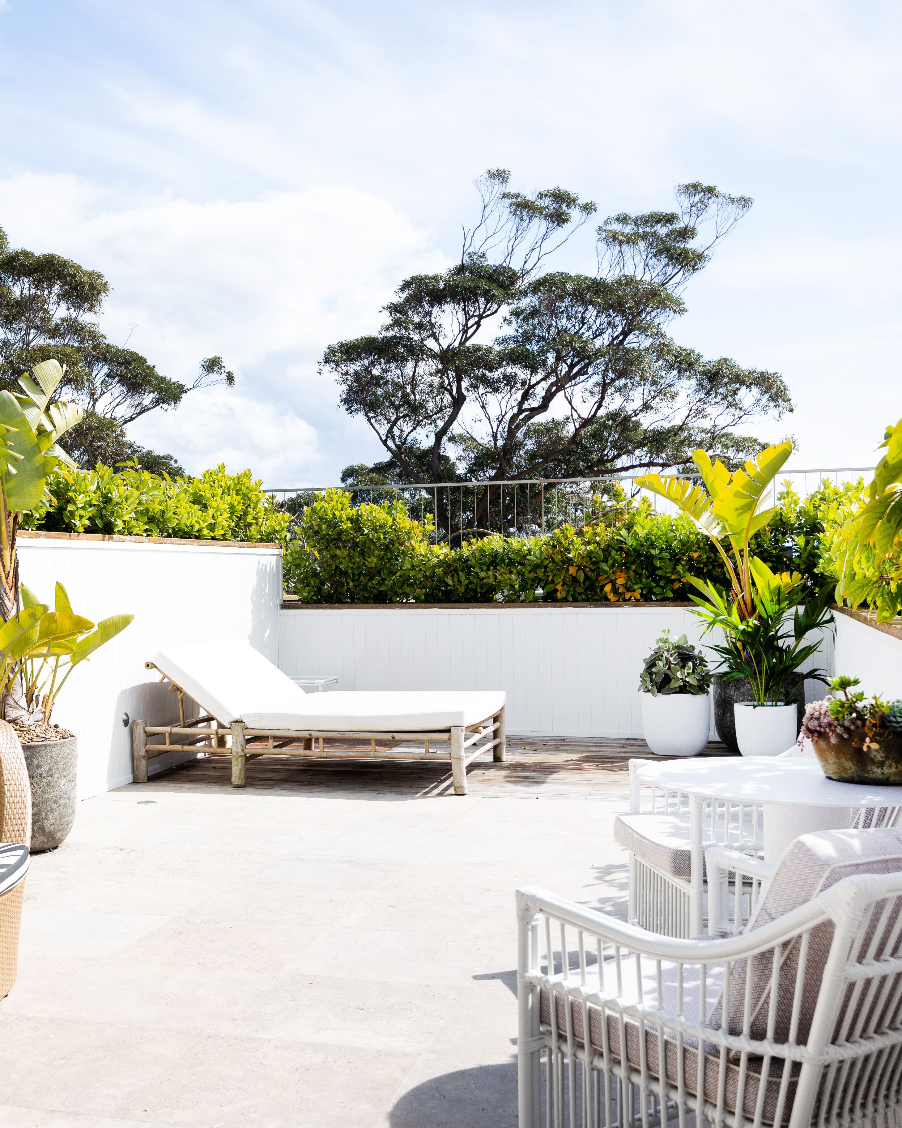 A rooftop patio with a white lounge chair, a small table, and potted plants.