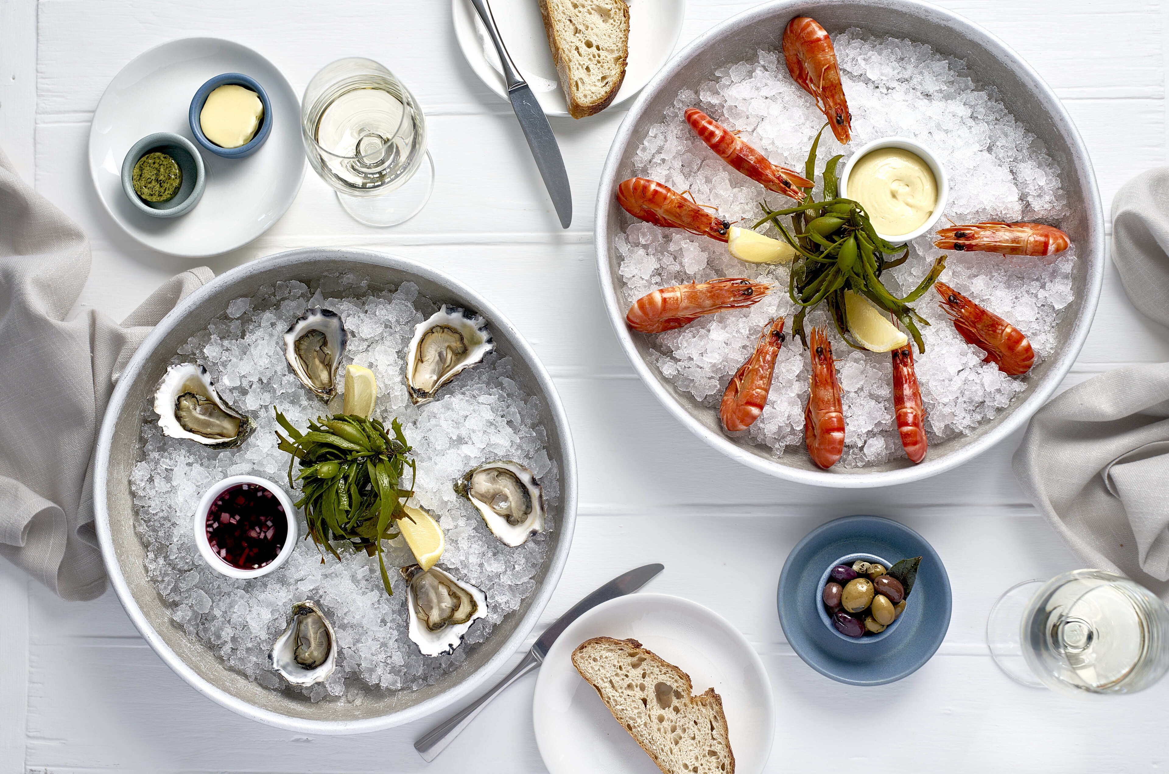 Twee schotels met zeevruchten op ijs, met oesters, garnalen en brood.