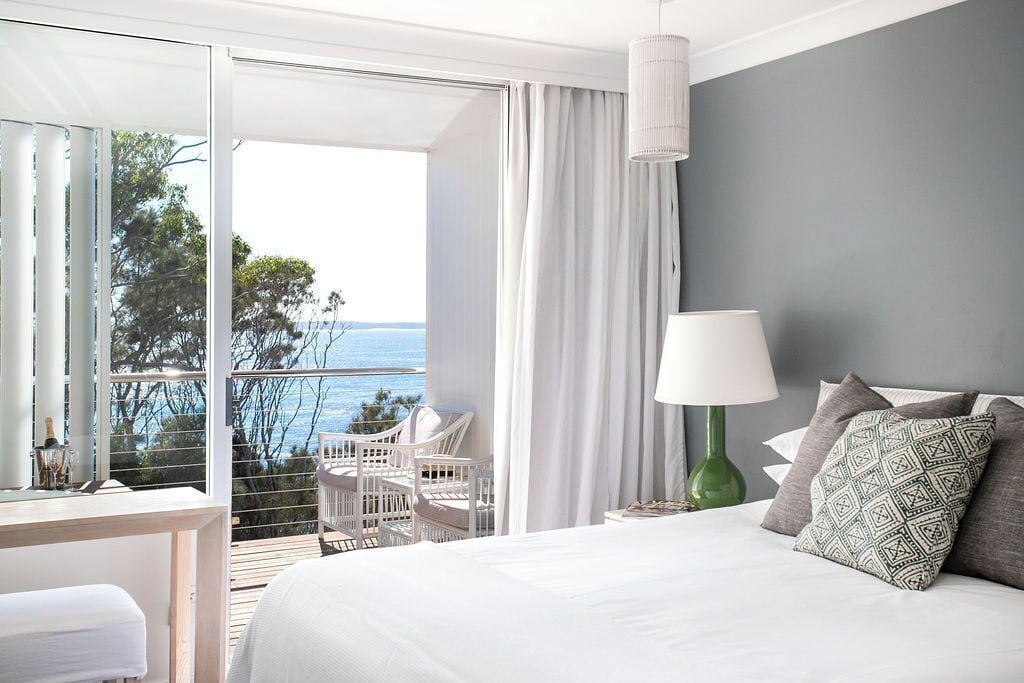 A hotel room with a balcony, a bed, a desk, and a chair.