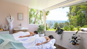 A spa room with two beds, a sink, and a view of the sea.