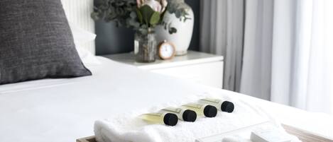 A neatly made bed with white linens, a wooden tray with folded towels, and a small vase with flowers on a bedside table.