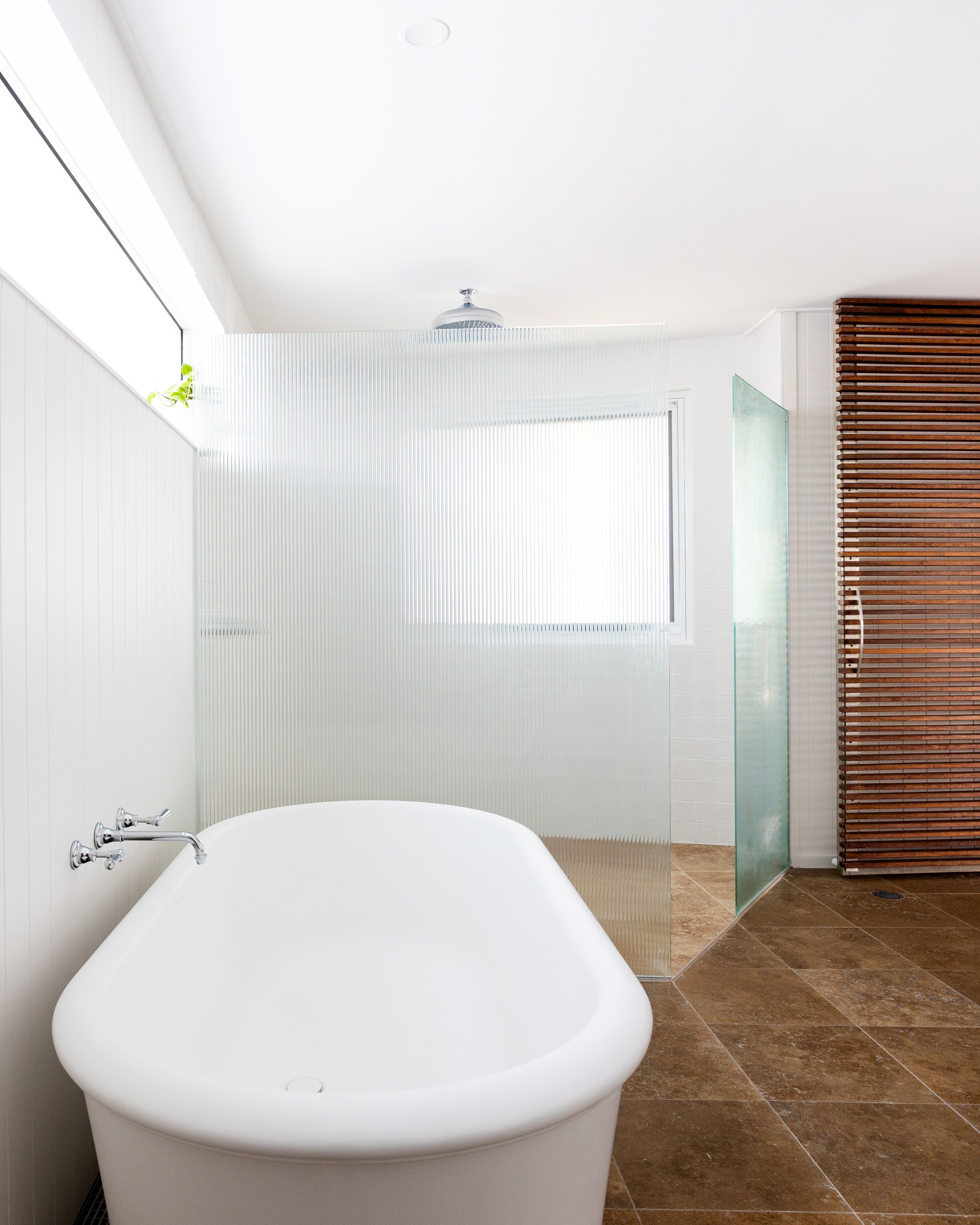 A modern bathroom with a freestanding bathtub, a glass shower enclosure, and a wooden blind.