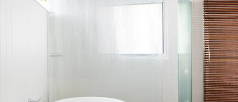 A modern bathroom with a freestanding bathtub, a glass shower enclosure, and a wooden blind.