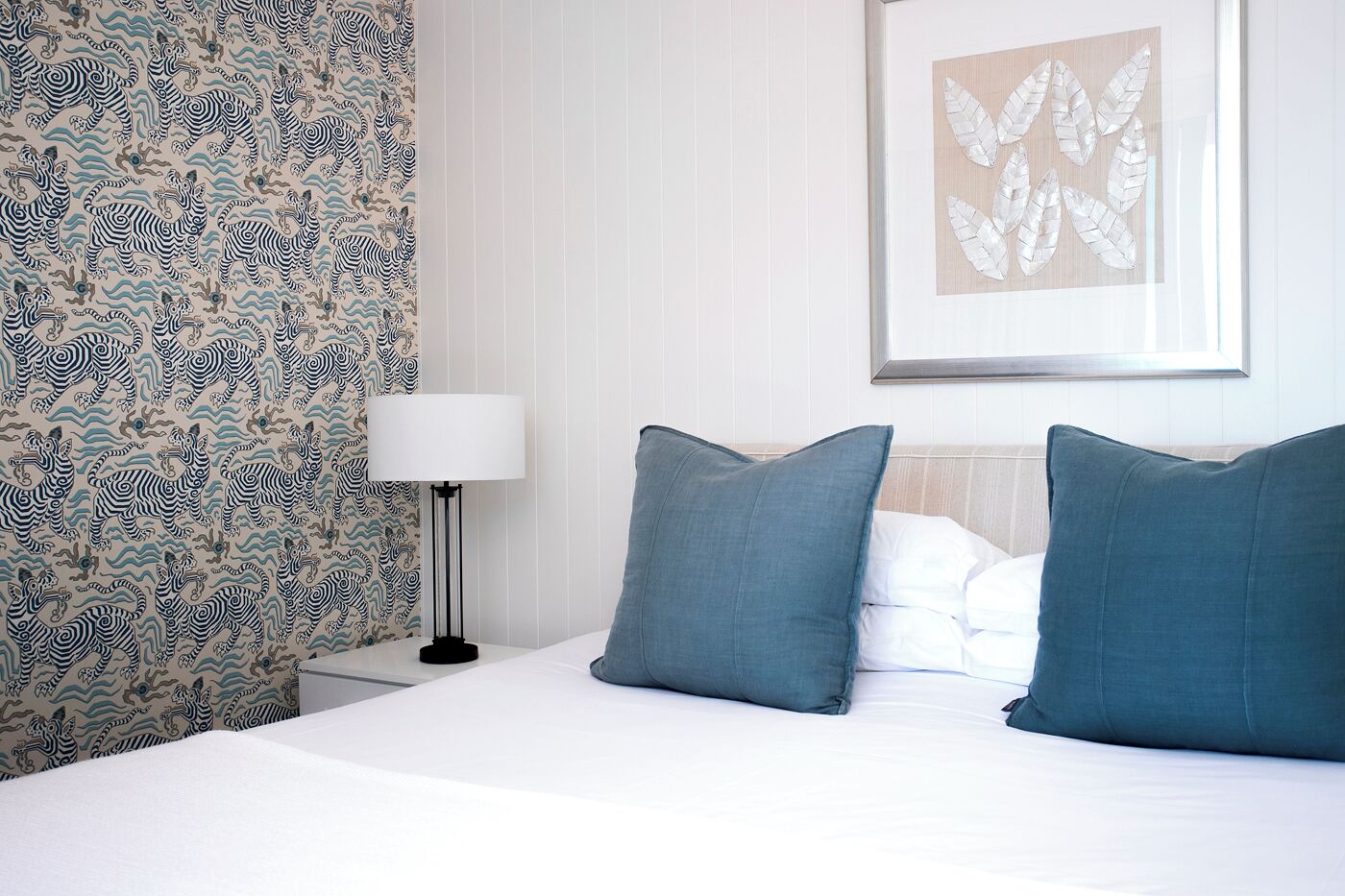 A hotel room with a bed, two pillows, a nightstand, a lamp, and a wall with a leaf pattern.