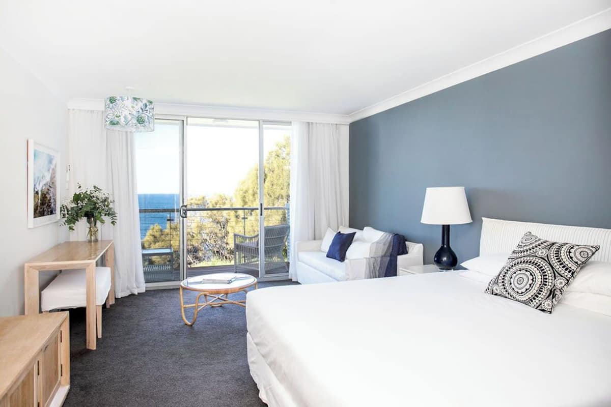 Ein Hotelzimmer mit Bett, Schreibtisch, Stuhl, Lampe und Blick ins Freie.