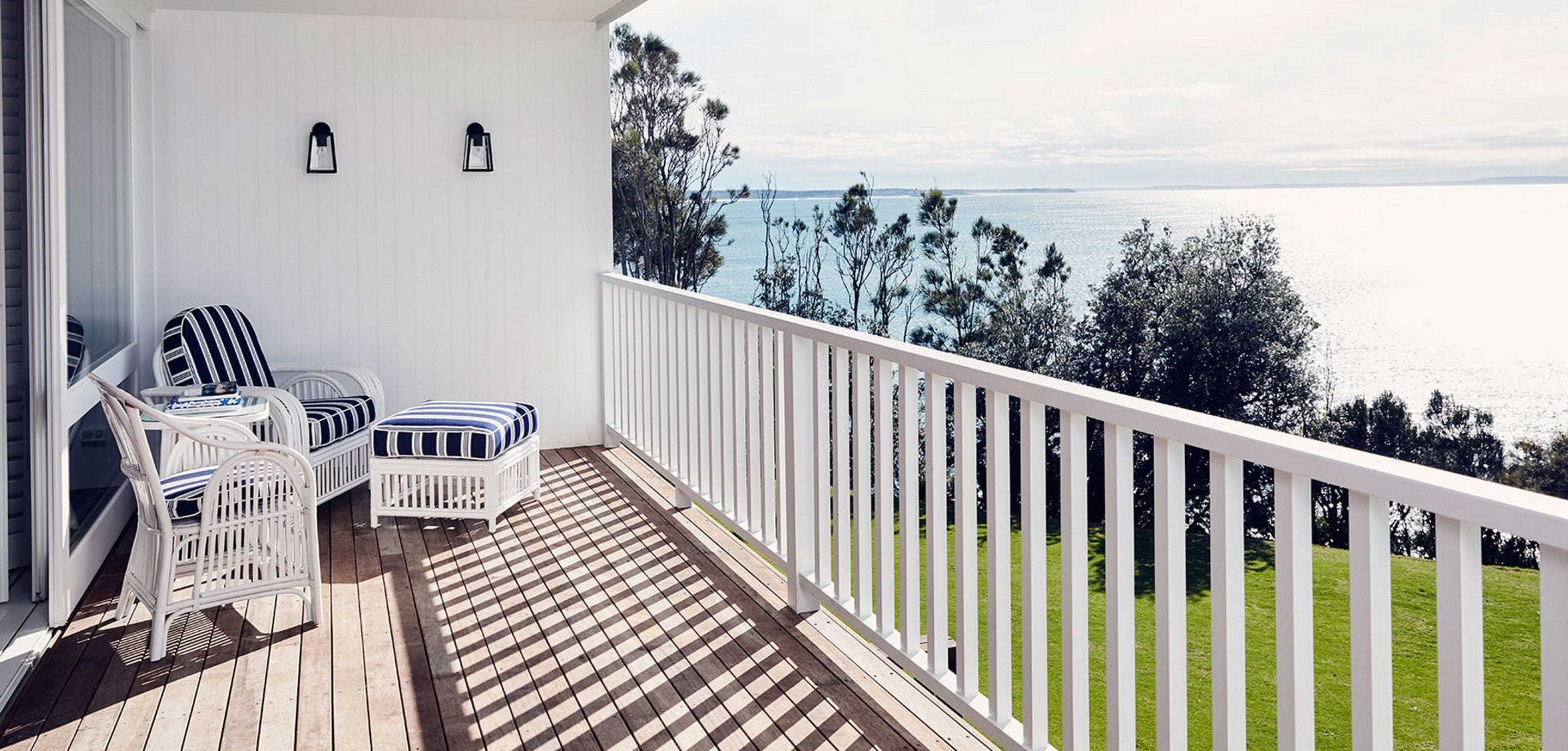 A balcony with white railings, two white wicker chairs, and a small table with a striped cushion.