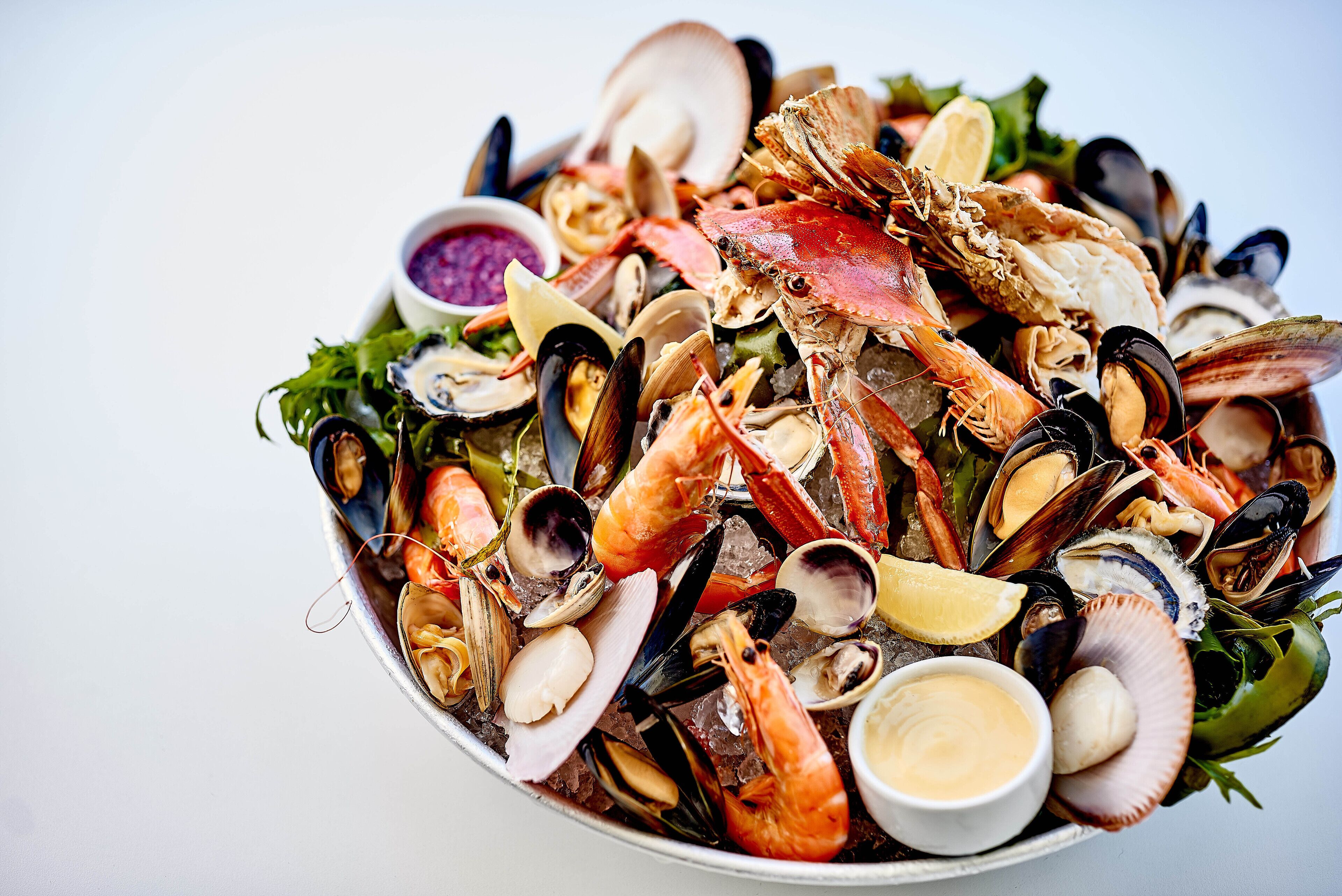 A seafood platter with various shellfish and a small bowl of sauce.