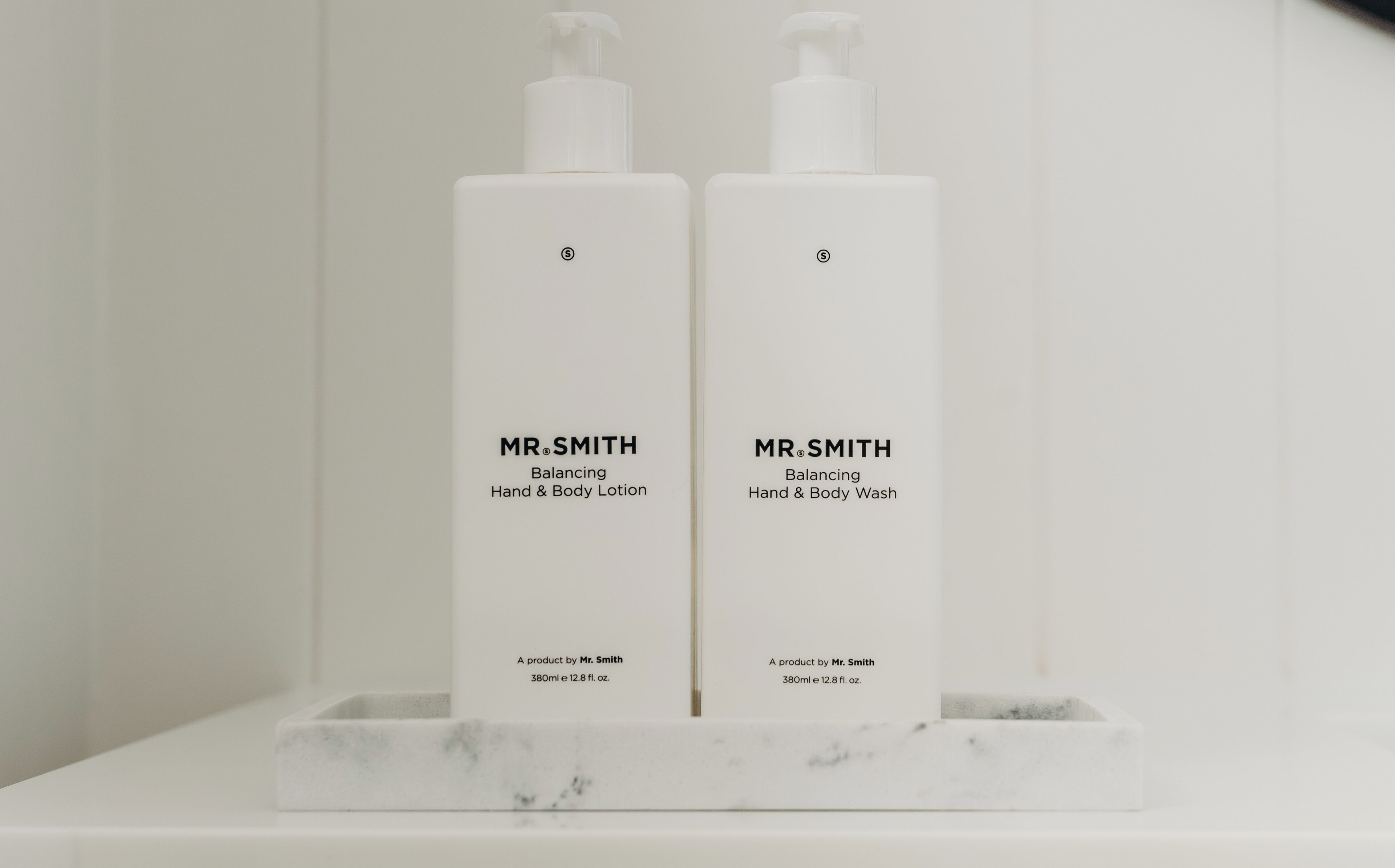 Deux personnes portant le nom de famille Smith, tenant en équilibre des flacons de crème pour les mains et de lotion pour le corps sur une étagère en marbre.