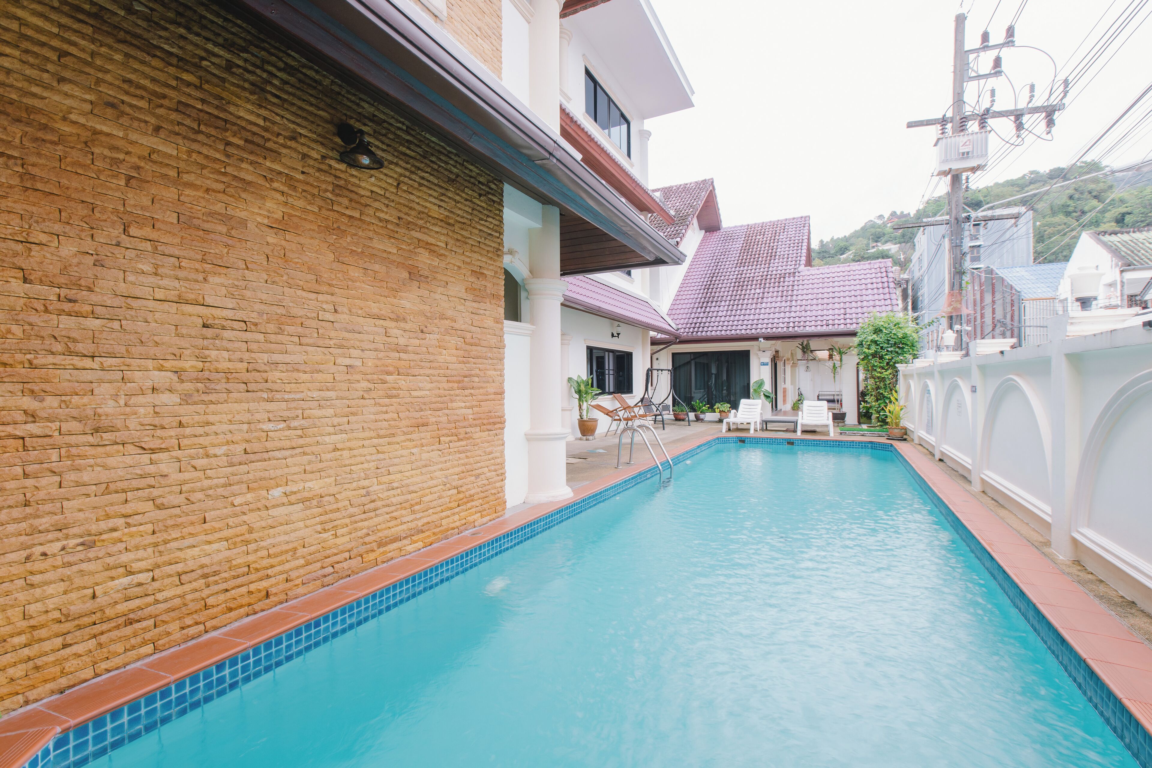 A swimming pool with a tiled edge, surrounded by a brick wall and a white fence.