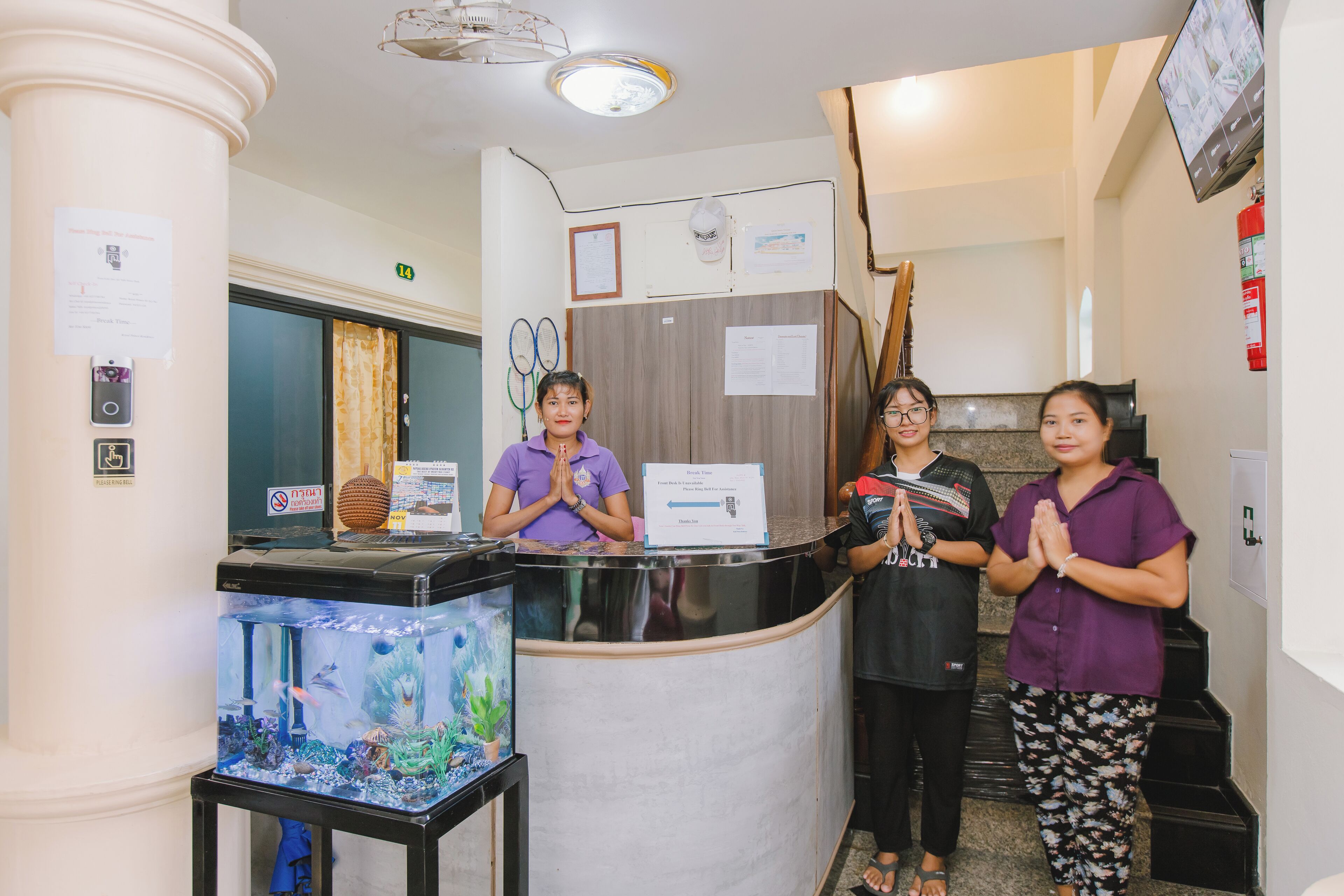 A reception desk with three staff members standing behind it, a fish tank, and a fire extinguisher on the wall.