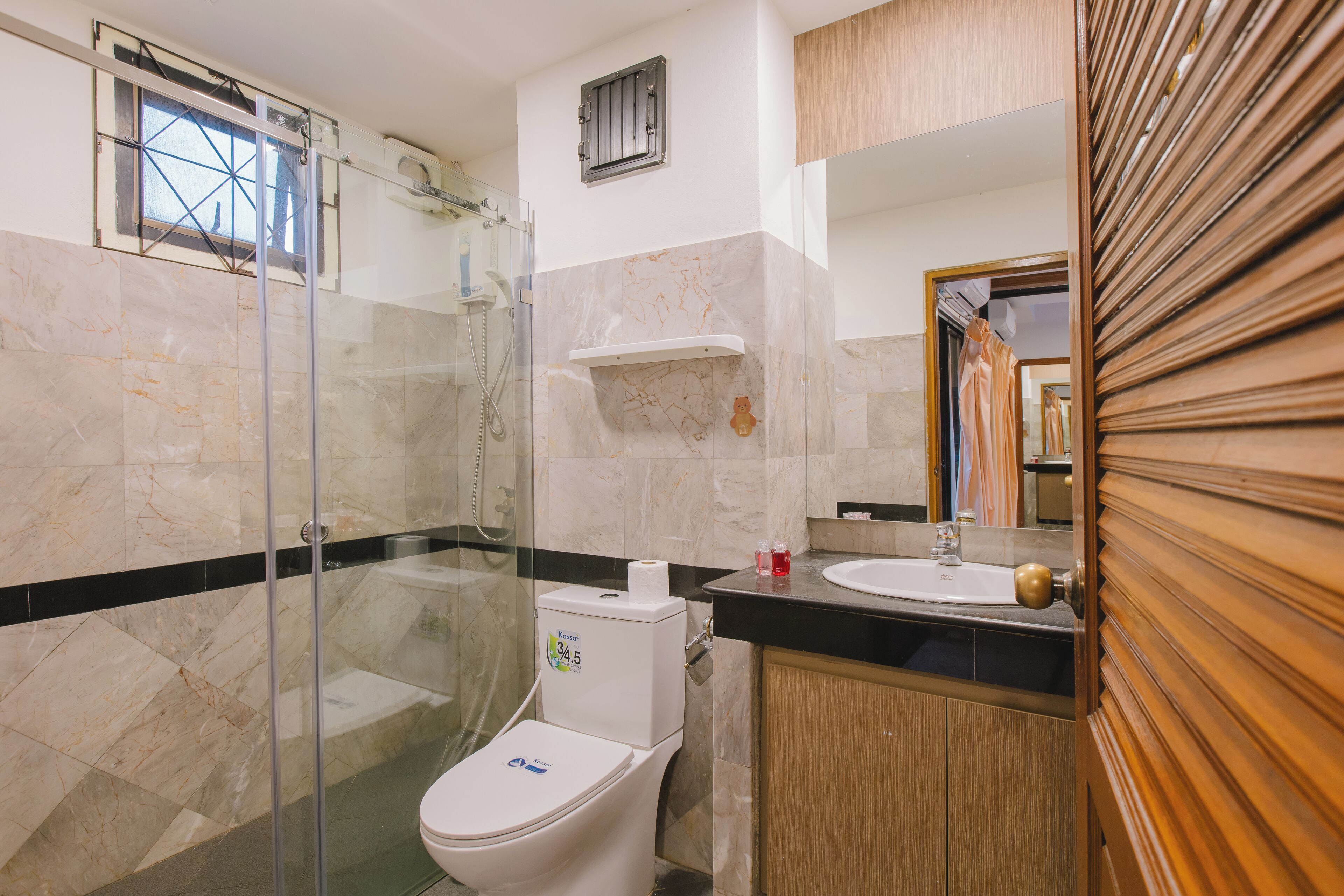 A bathroom with a glass shower enclosure, a toilet, a sink, and wooden cabinets.