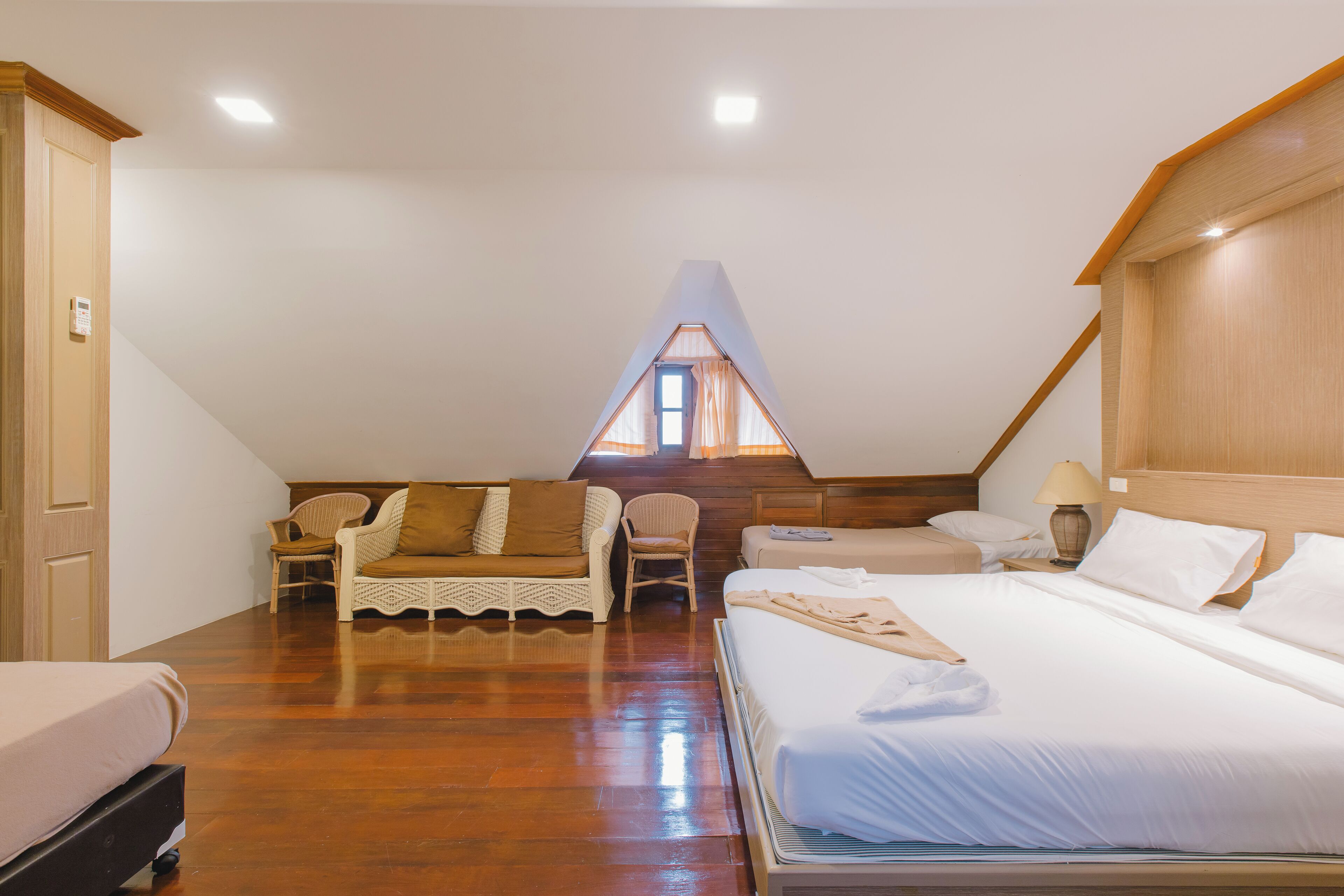 Quarto com teto inclinado, uma cama, um sofá e uma cadeira.