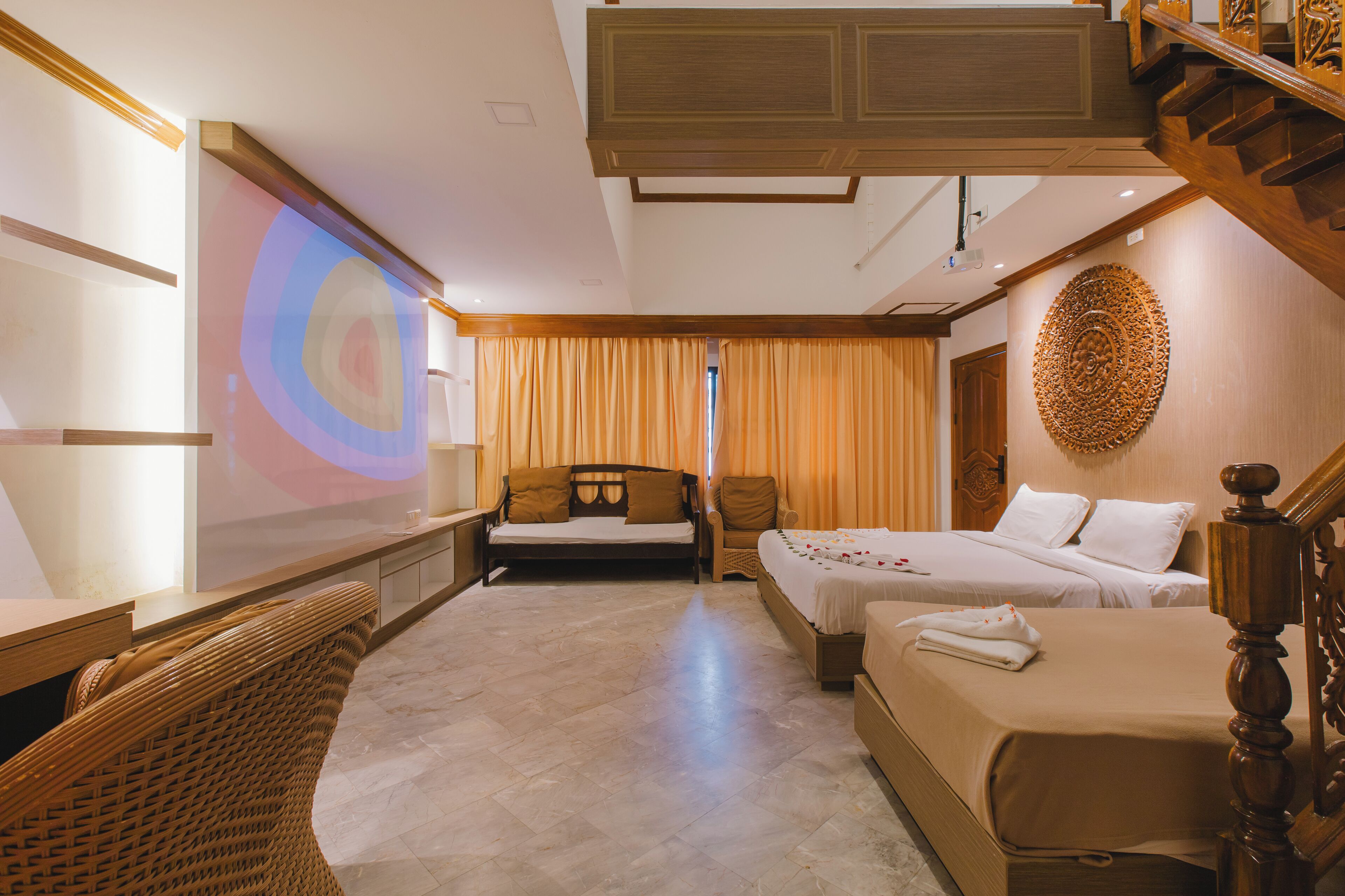 A hotel room with a large bed, a smaller bed, a sofa, a chair, and a wooden staircase.