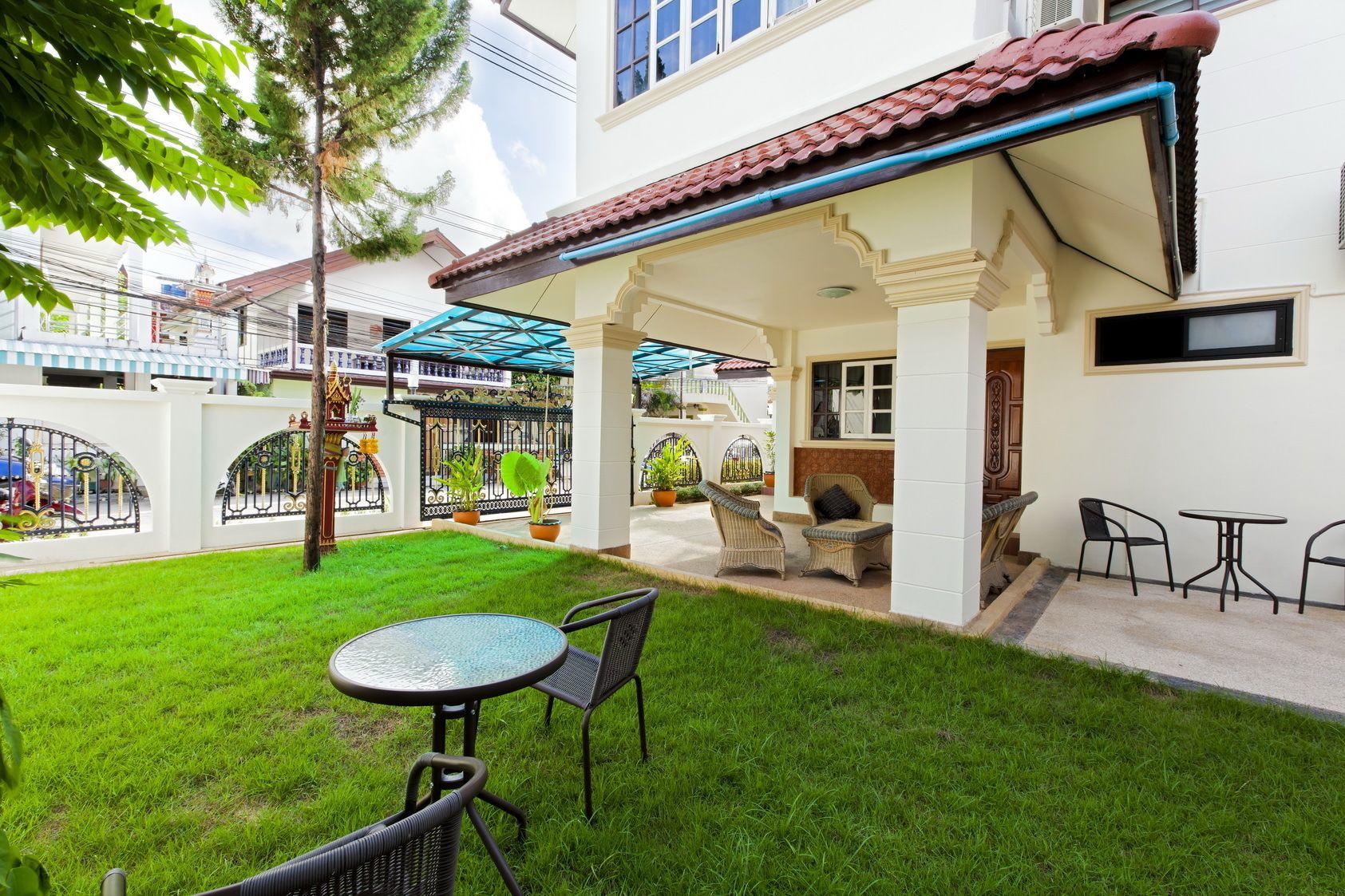 A covered outdoor seating area with chairs and a table, surrounded by a well-maintained lawn and potted plants.