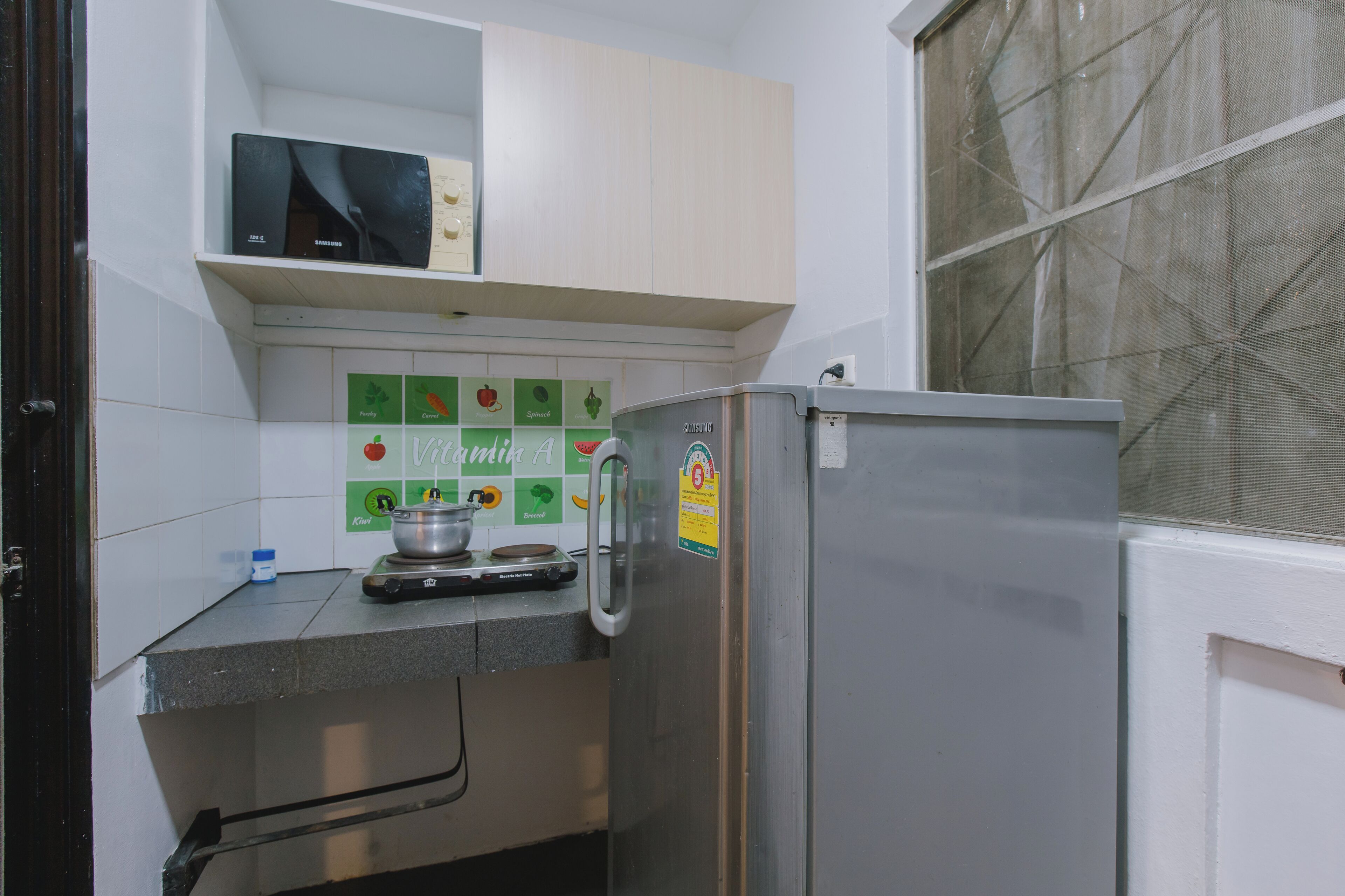 A kitchen with a stainless steel refrigerator, a microwave, and a tiled backsplash with fruit illustrations.