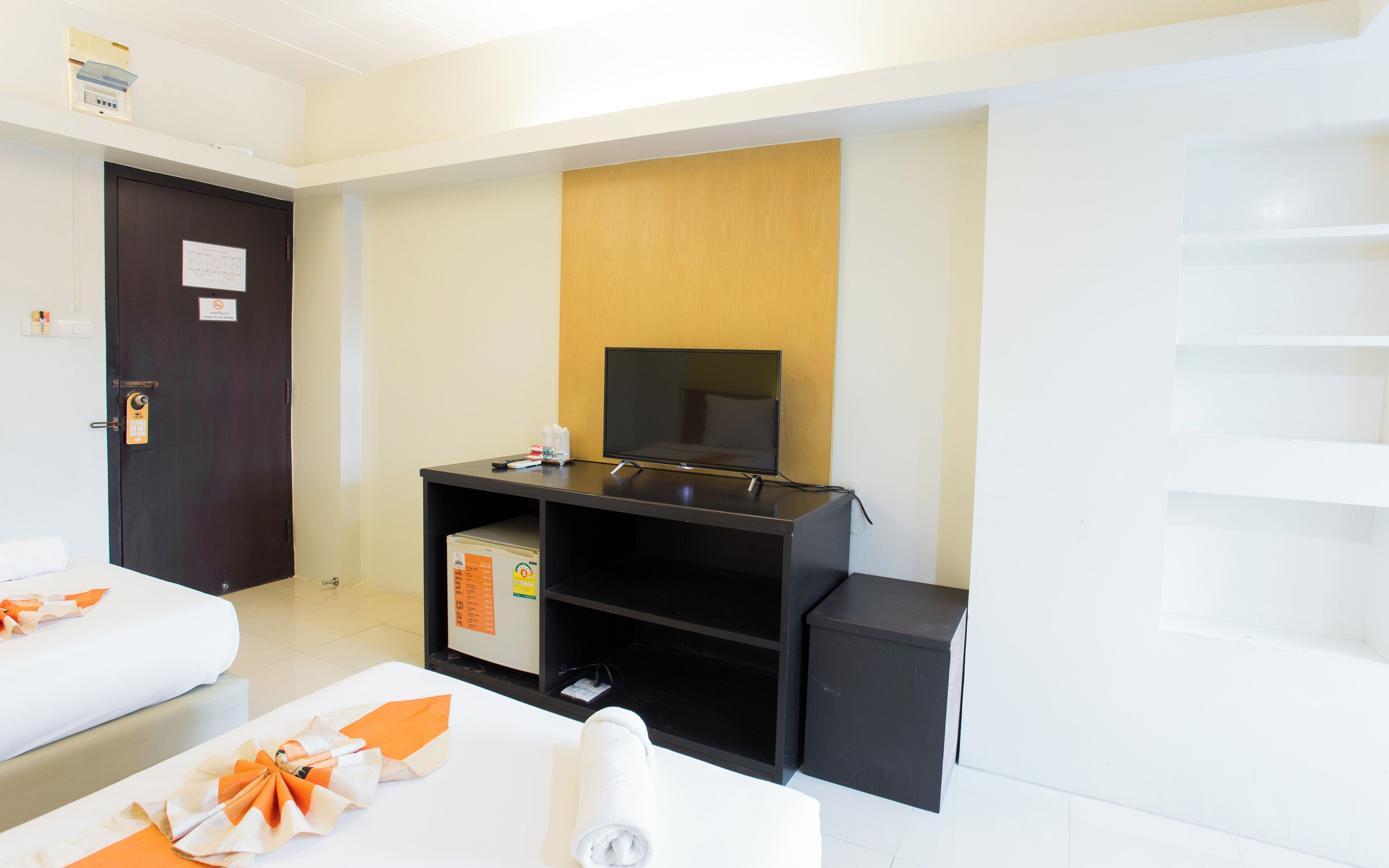 A hotel room with a bed, a TV on a stand, a small desk, and a wooden panel on the wall.