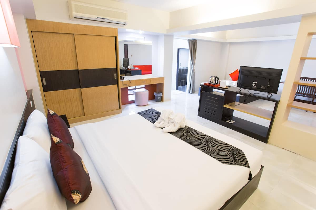 A modern hotel room with a large bed, a wardrobe, a desk with a computer, and a television.