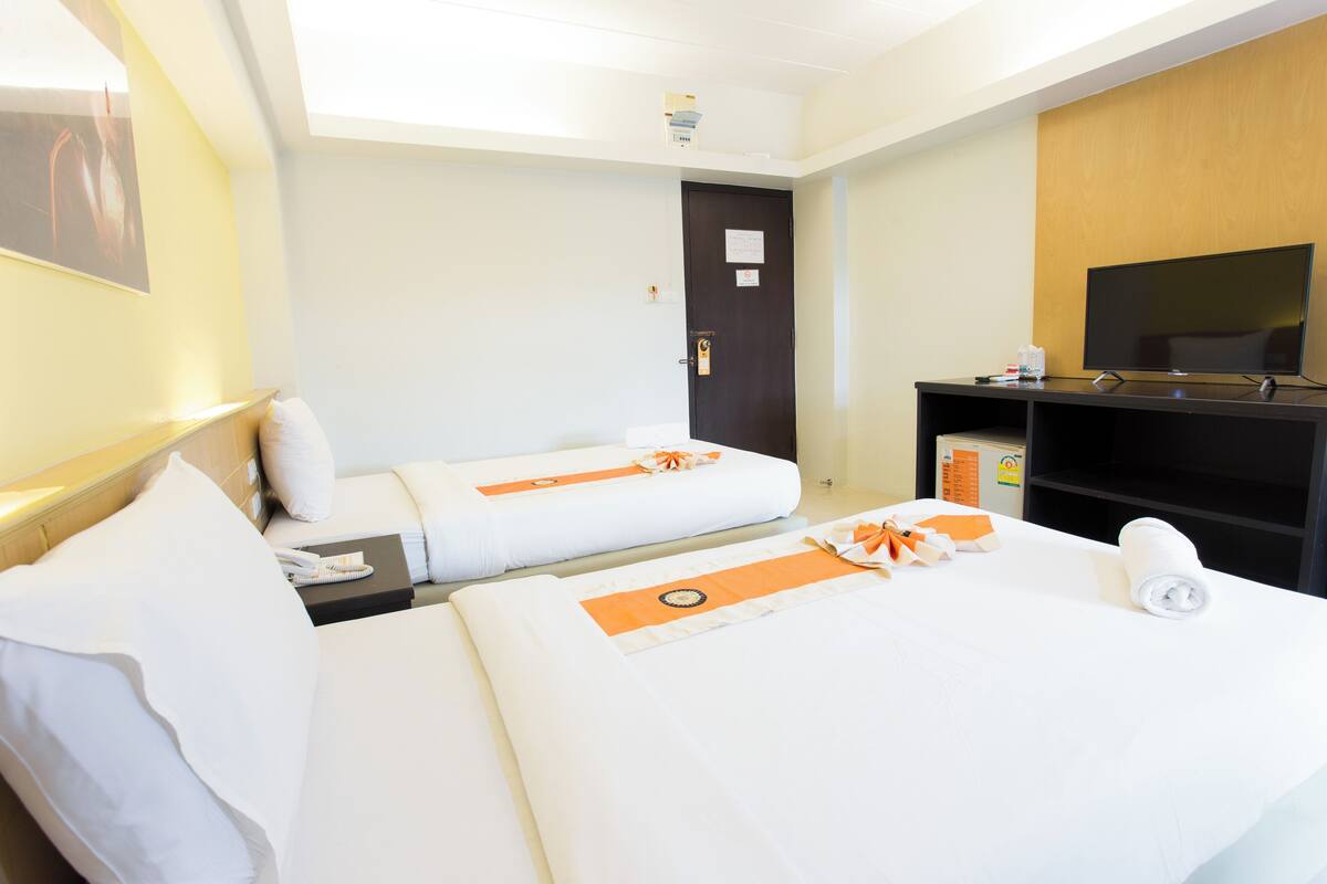 A hotel room with two beds, a TV, a desk, and a door.