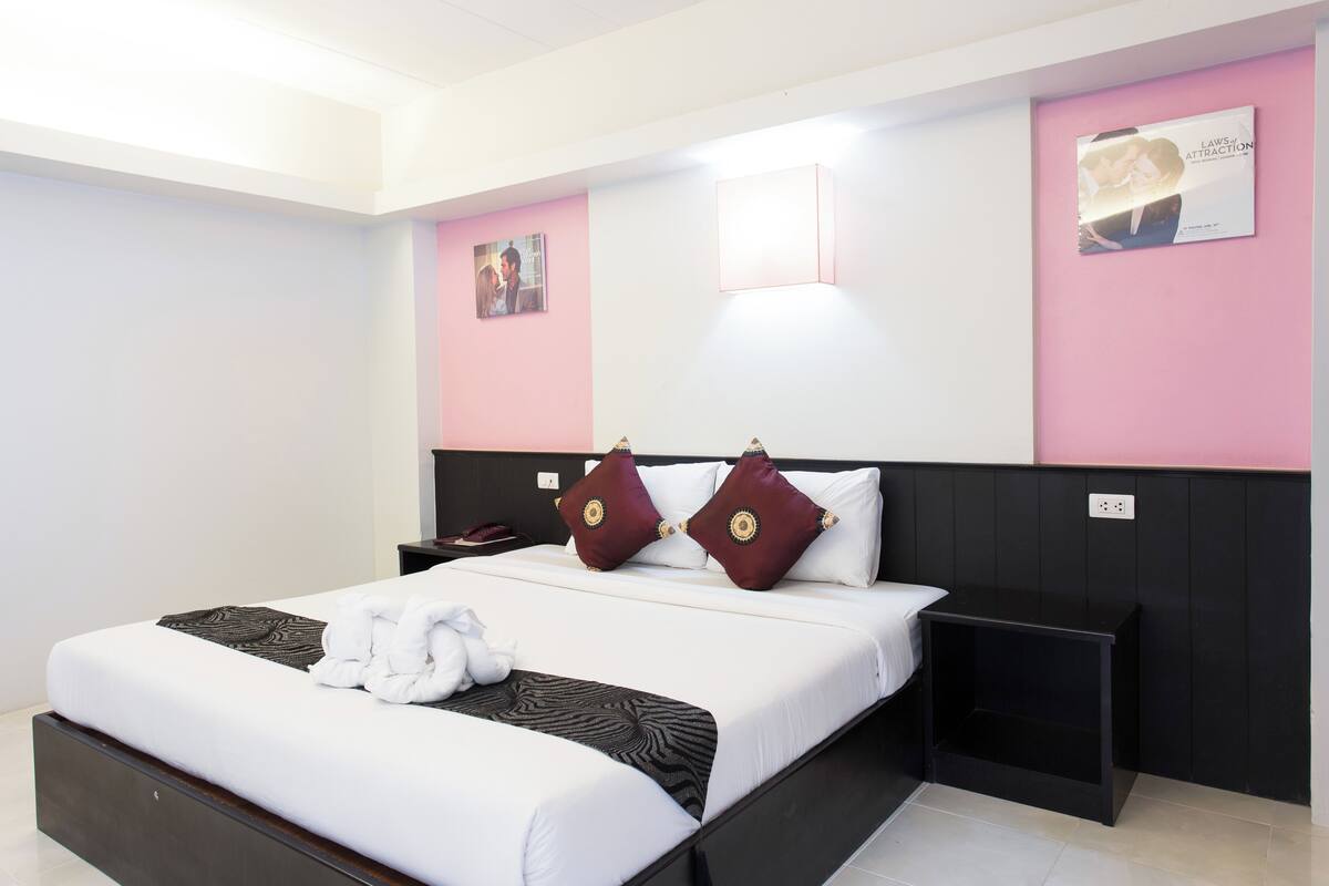 A hotel room with a large bed, a bedside table, a nightstand, a wall-mounted light, and a framed picture.