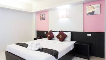 Une chambre d’hôtel avec un grand lit, une table de chevet, une commode, une lampe fixée au mur et un tableau encadré.
