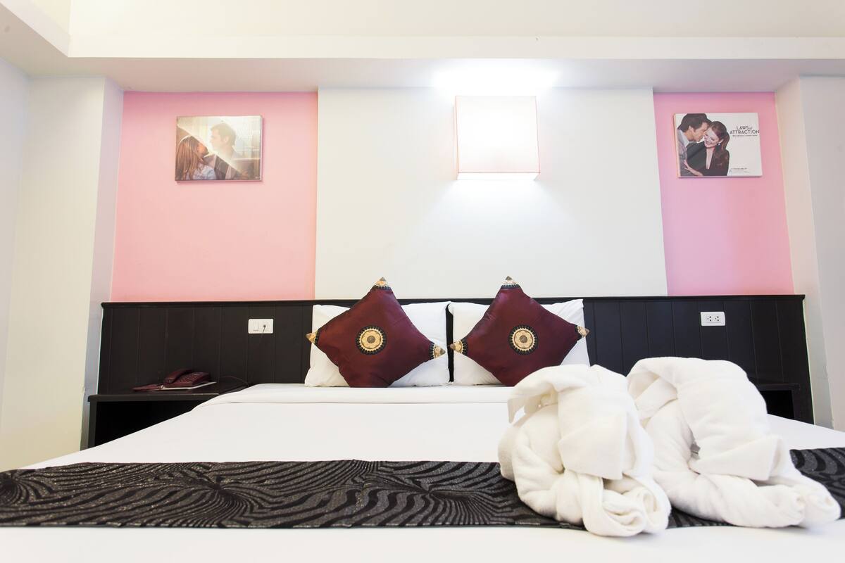 A hotel room with a bed, two pillows, a bedside table, and a wall-mounted picture.