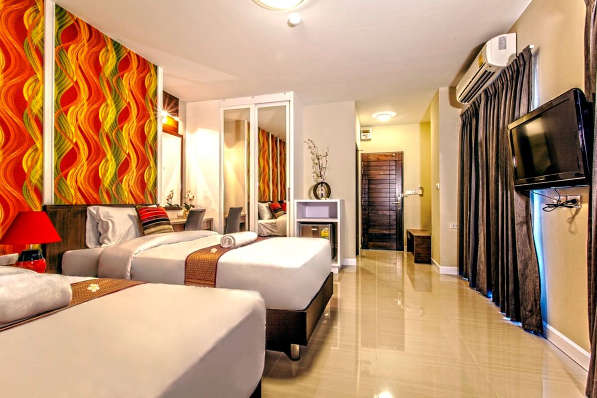 A hotel room with two beds, a TV, an air conditioning unit, and a mirror.