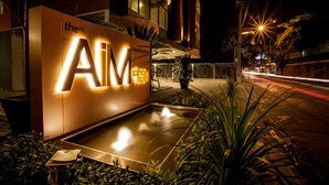 A hotel entrance with illuminated signage, a paved area, and surrounding greenery. - The Aim Sathorn Hotel (Bangkok)
