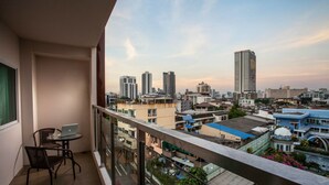 A balcony with a laptop on a table, overlooking a cityscape with various buildings and a clear sky. - The Aim Sathorn Hotel (Bangkok)