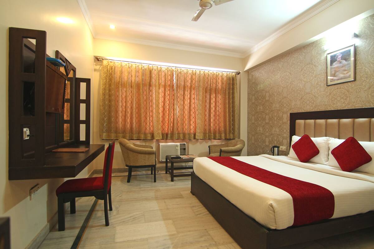 A hotel room with a bed, a desk, two chairs, a small table, and a window with curtains.