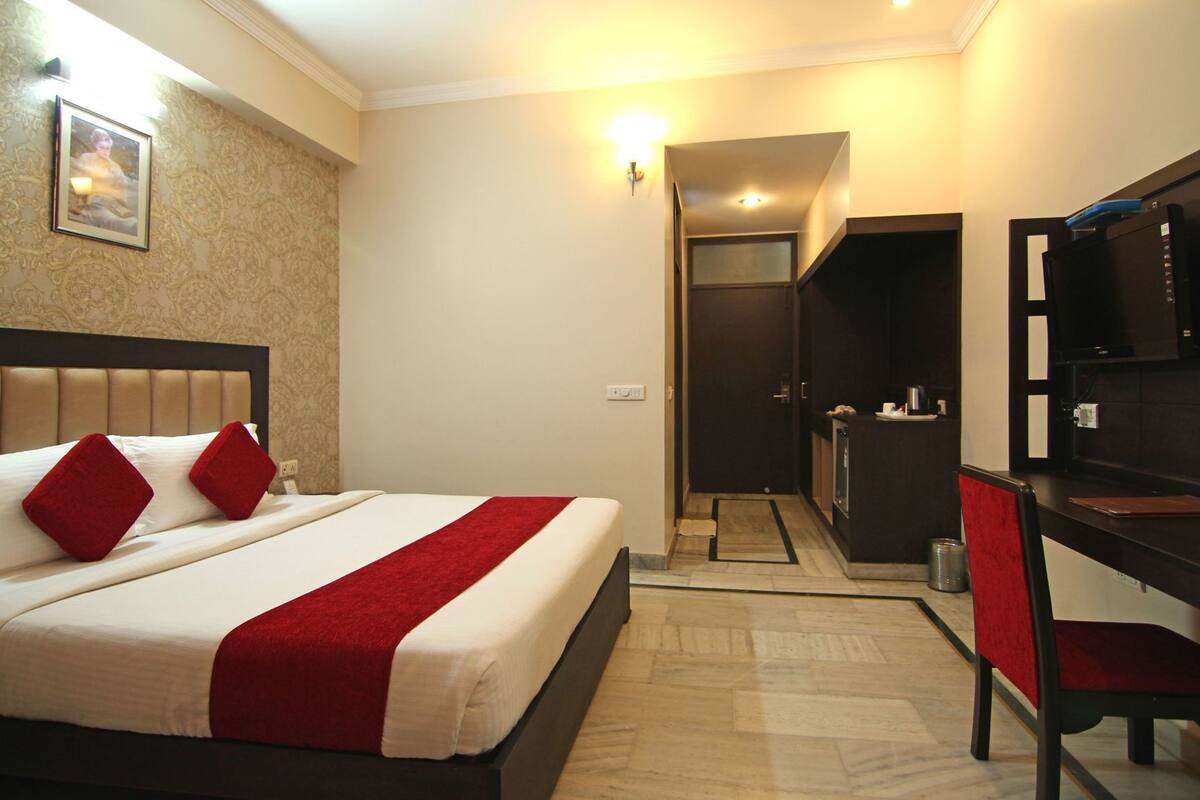 A hotel room with a bed, a desk, a chair, a television, and a door leading to a bathroom.