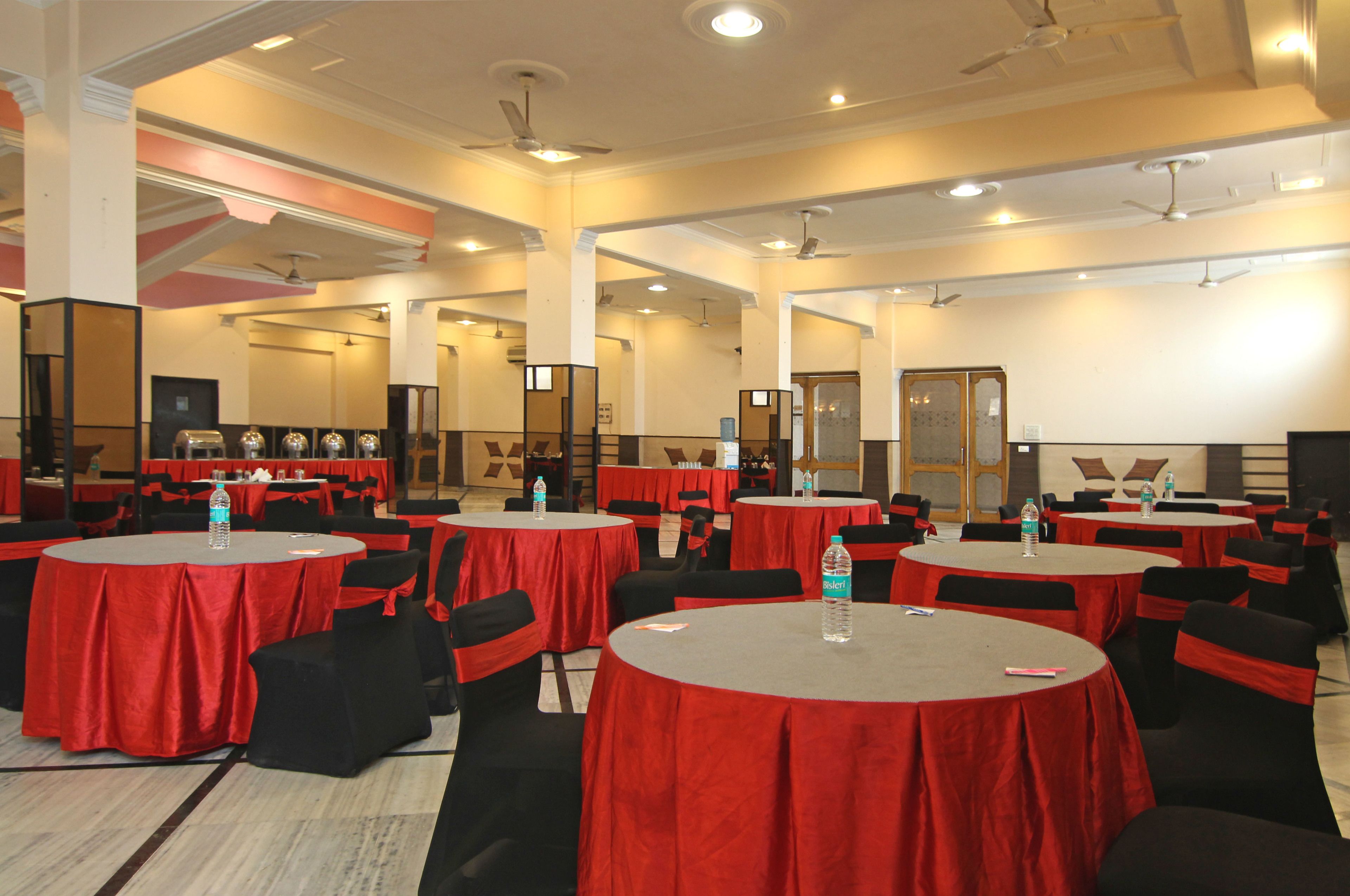 A conference room with multiple round tables covered in red tablecloths, black chairs, and water bottles.