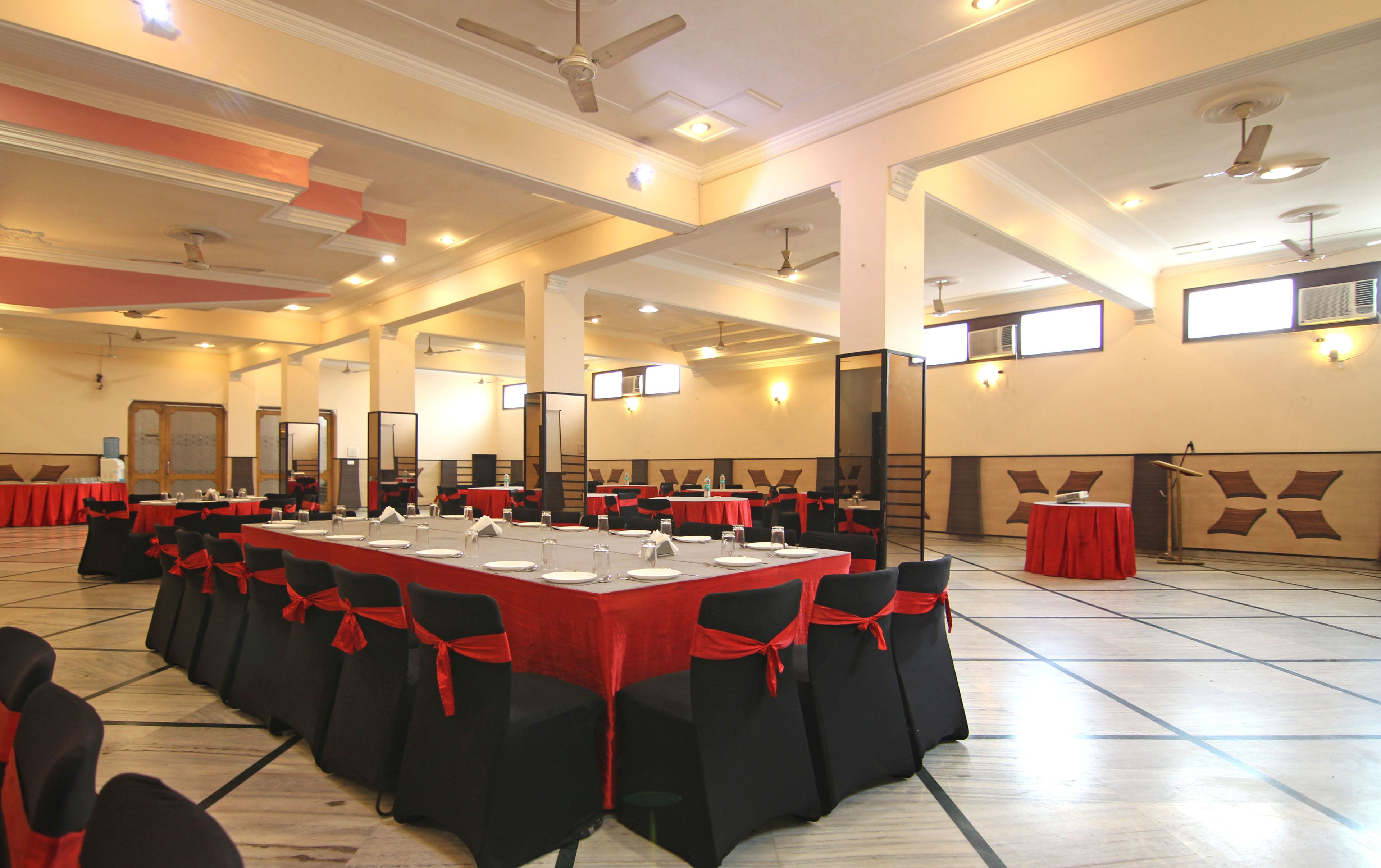 A large conference room with tables set for a meeting, black chairs with red sashes, and ceiling fans.