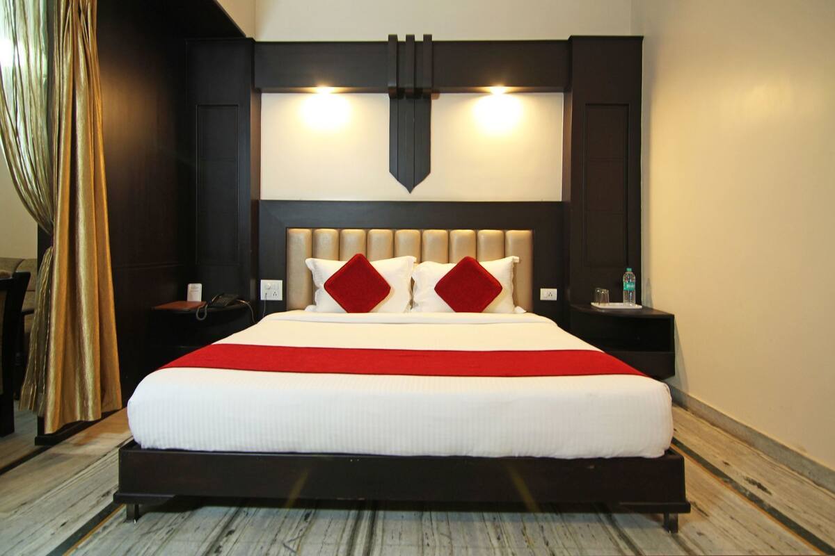 A hotel room with a large bed, two bedside tables, a headboard with integrated lighting, and a red accent pillow.