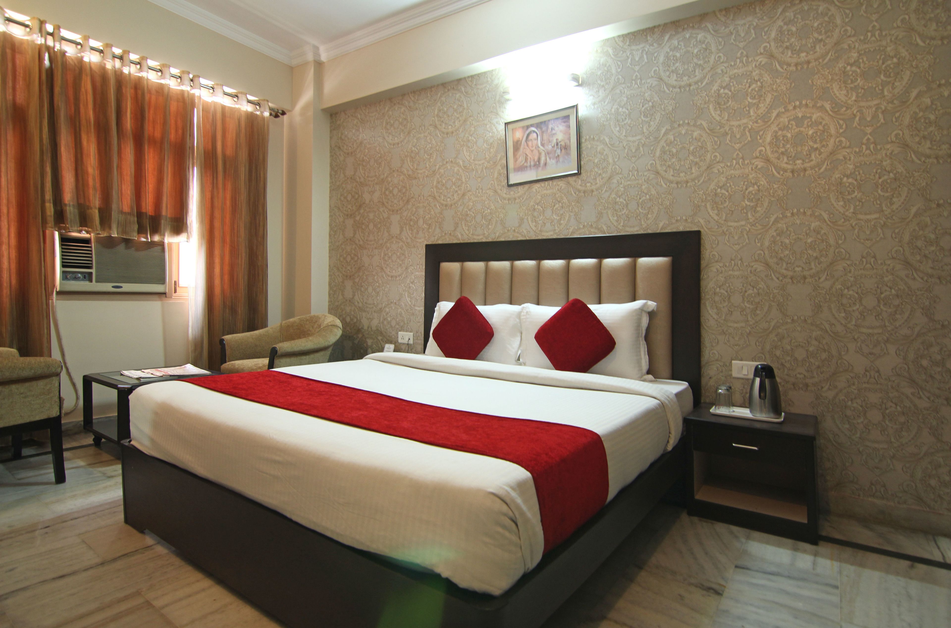 A hotel room with a large bed, a bedside table with a lamp, a chair, and a window with curtains.