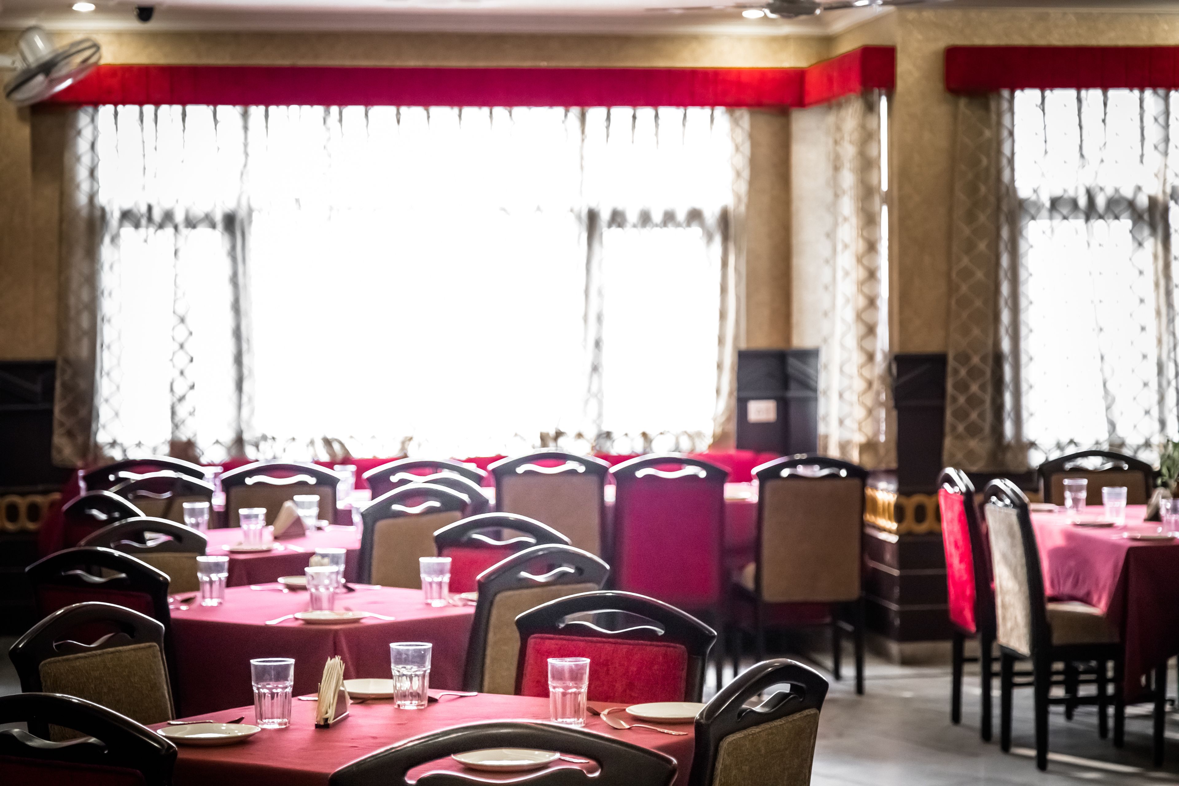 A restaurant with multiple tables and chairs, red tablecloths, and a bright interior.