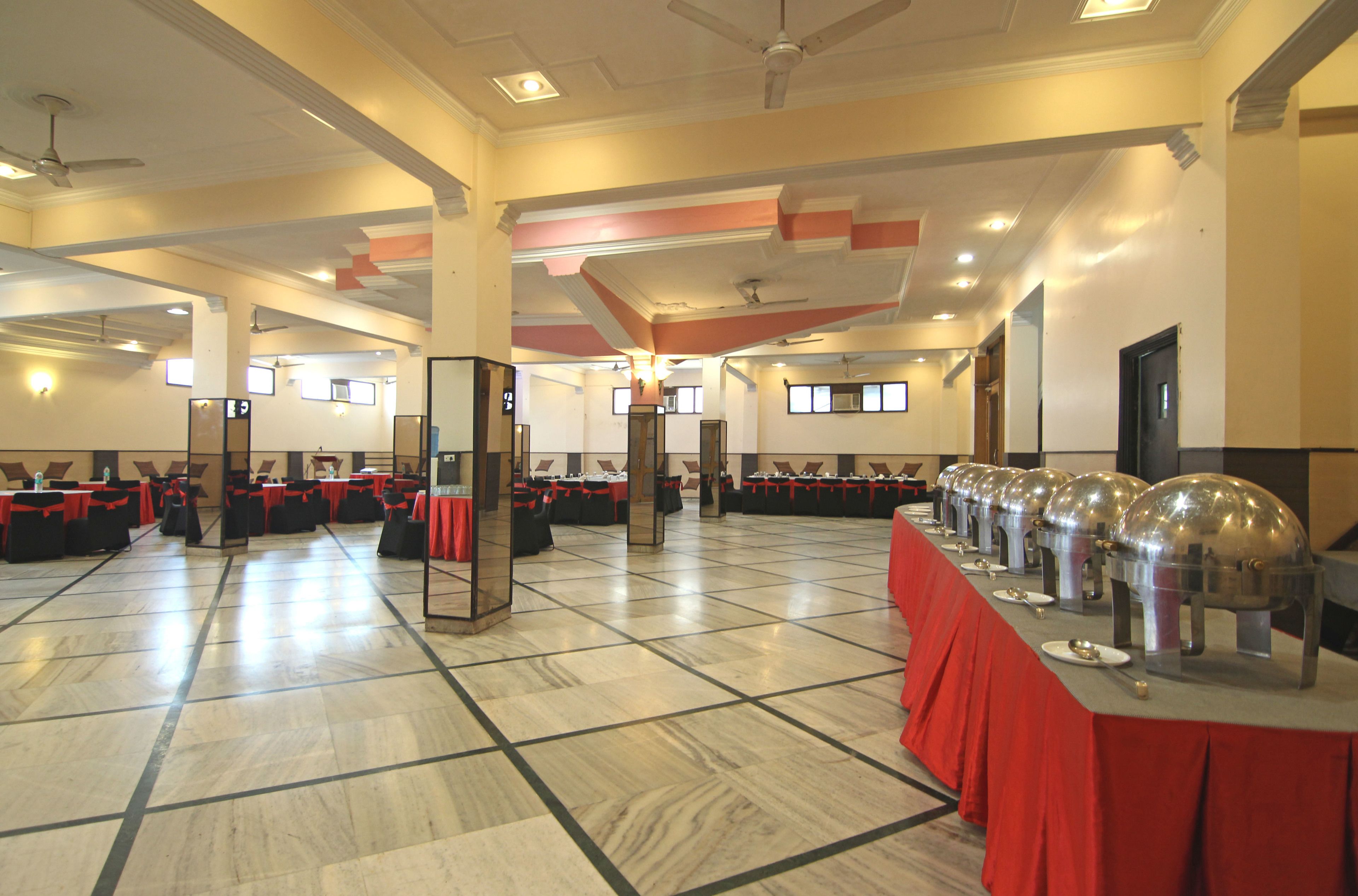 A spacious hall with rows of tables and chairs, ceiling fans, and a long buffet table with food service equipment.