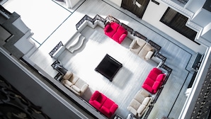 Et rummeligt loungeområde med et centralt, sort sofabord omgivet af fire røde sofaer og fire beige lænestole. Rummet har et moderne design med et lyst gulv og mørke trædetaljer.