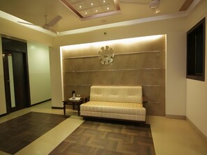 A modern hotel room with a sofa, a small table, and a decorative wall panel. - Hotel Poonam (Mahabaleshwar)