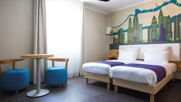 Habitación de hotel con cama, dos sillones azules, una mesita y un mural con vistas urbanas en la pared.