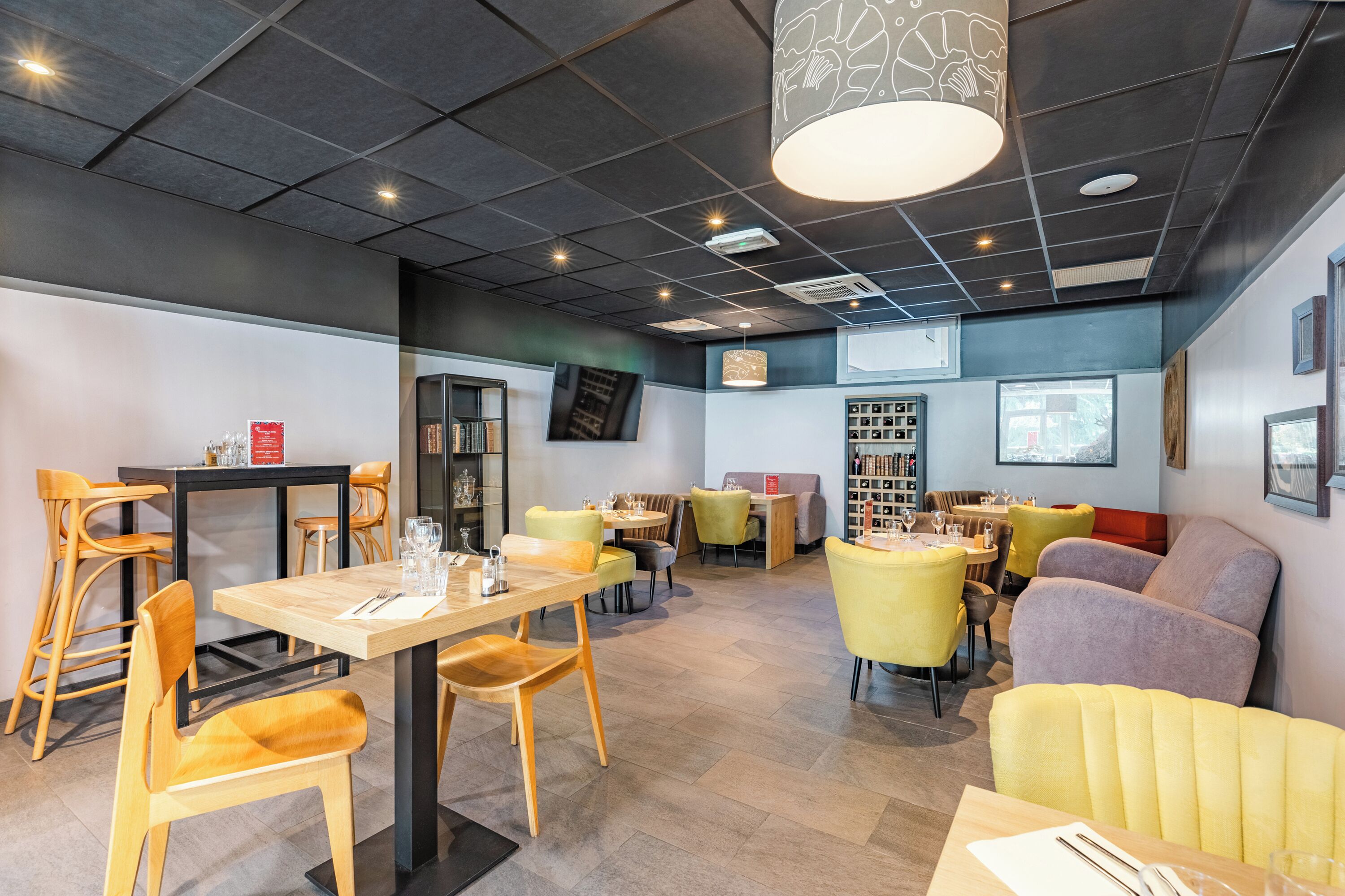 Un restaurant moderne avec un intérieur élégant, des tables et des chaises en bois, un espace central dédié à la restauration et un coin salon avec des fauteuils confortables.